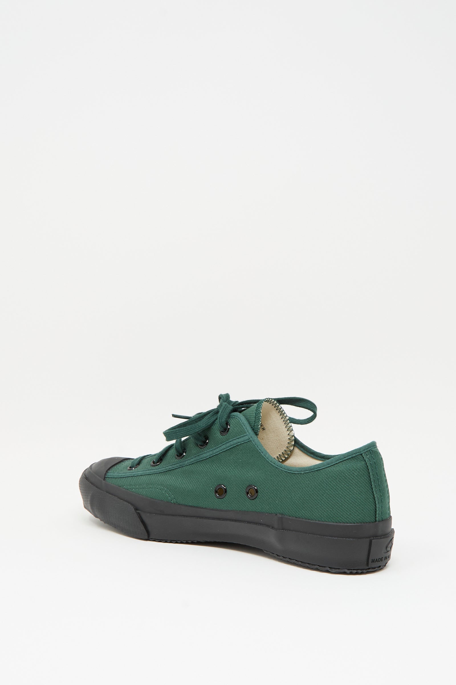 The Moonstar Gym Classic Sneaker in Dark Green features a green canvas low-top design, black rubber sole, and black eyelets, shown from the side against a plain white background.