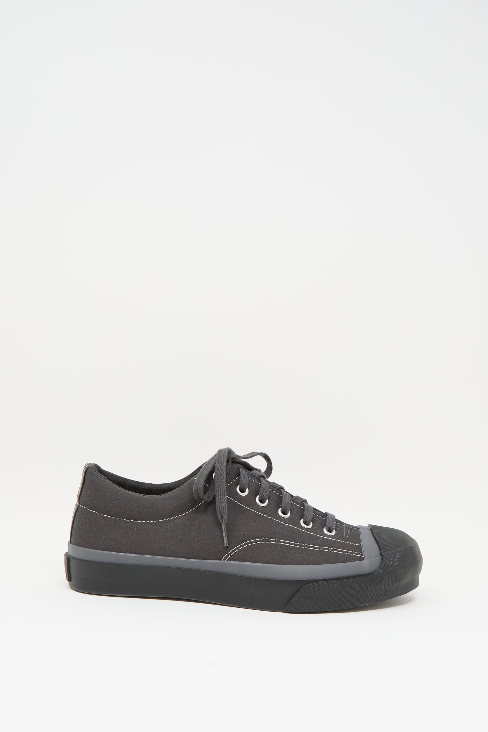The Moonstar Gym Court Sneaker in Charcoal is a black low-top crafted from cotton nylon canvas with matching laces and a rubber toe cap, shown in side view against a plain white background.