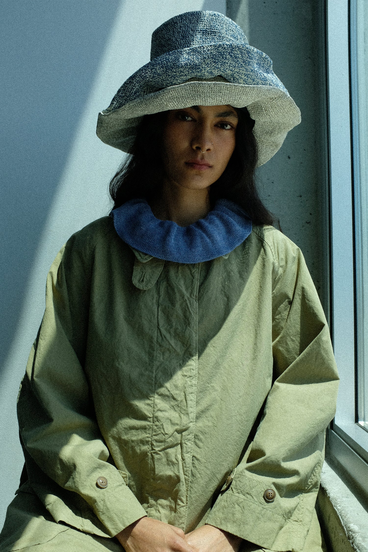 Person wearing Reinhard Plank Isle New Paper Hat stacked on top of each other, with the Supima Cotton Topcoat in Green sitting by a windowsill.