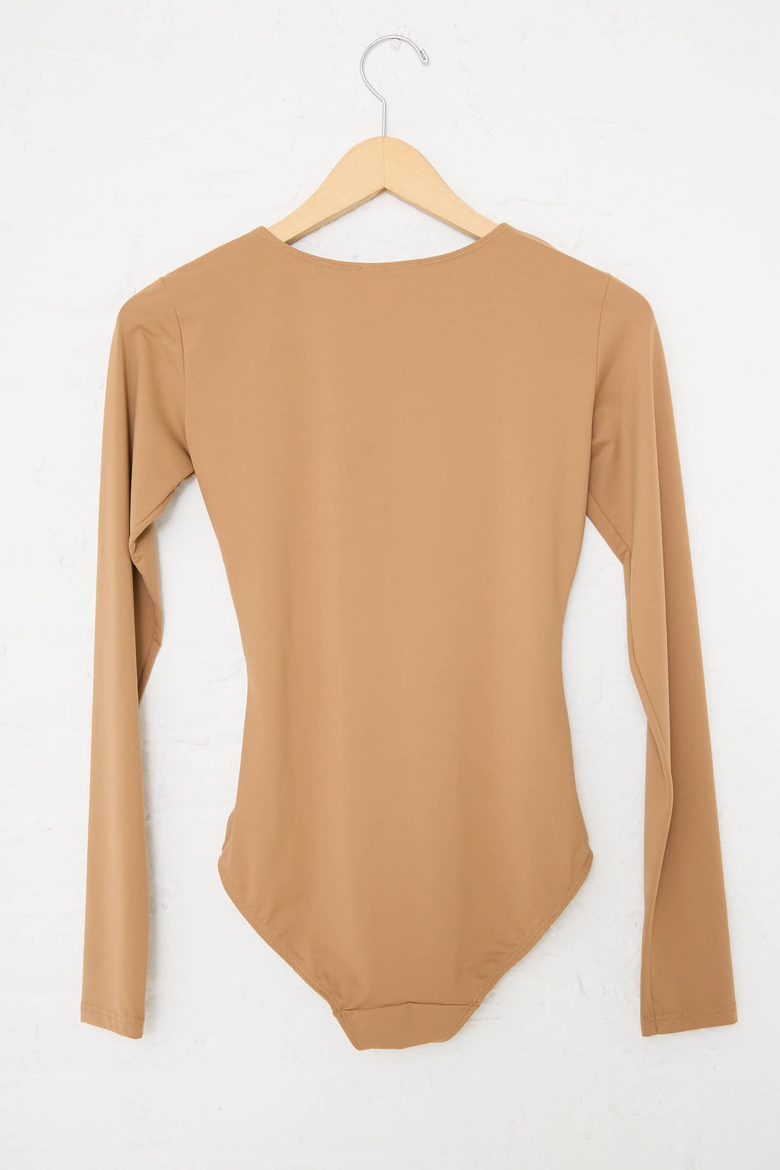 A Niccolò Pasqualetti Alix Sleeved Bodysuit in nude, featuring long sleeves and a slim-fit design made from stretch lycra, hangs neatly on a wooden hanger against a white wall with its back facing forward.