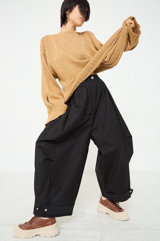 A woman accessorized in Niccolò Pasqualetti's Cotton Twill Luna Trouser in Black and a tan sweater. Full length and front view.