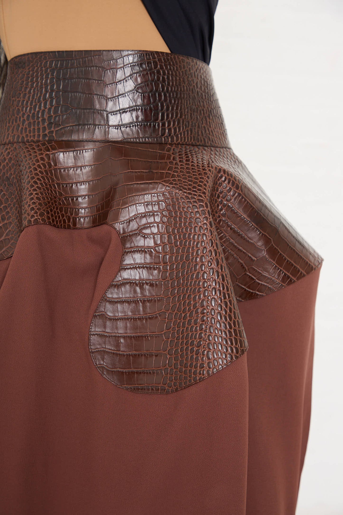 Close-up of the Niccolò Pasqualetti Croc Embossed Leather and Viscose Crepe Onda Skirt in Brown and Burnt Brown, featuring deep brown croc-embossed leather material combined with dark brown viscose crepe fabric. The design showcases structured detailing around the waist area.