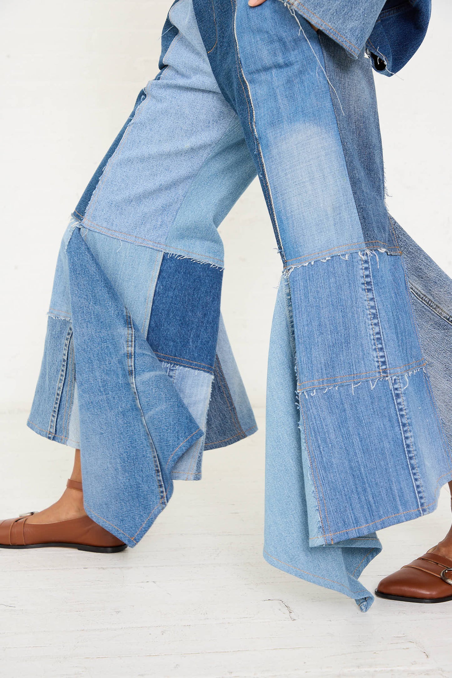 A person wearing Niccolò Pasqualetti's Salvaged Jean Patchwork Lengo Trouser in Blue and brown loafers walks with one foot slightly ahead of the other.