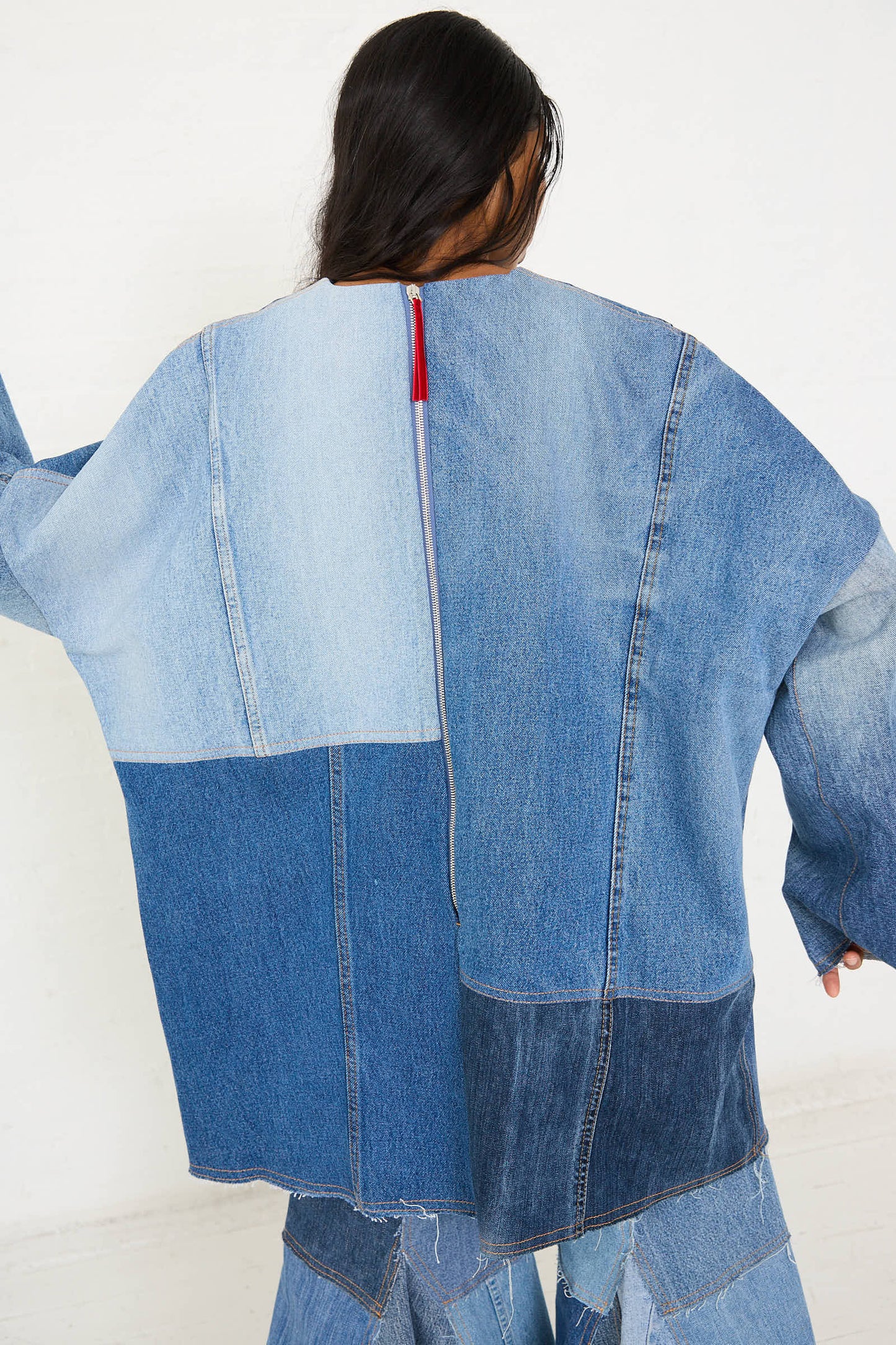 Person wearing an oversized Salvaged Jean Patchwork Raglan Shirt in Blue by Niccolò Pasqualetti, shown from the back. The long sleeves add a casual yet stylish touch to the overall look.