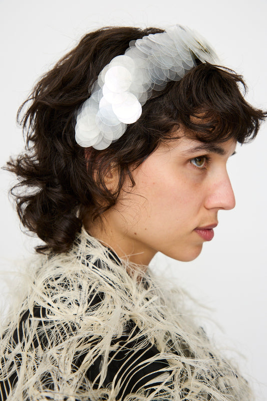 A person with short, wavy brown hair wears the Niccolò Pasqualetti Sfocatura Headband in Khaki and a feathered, textured garment.