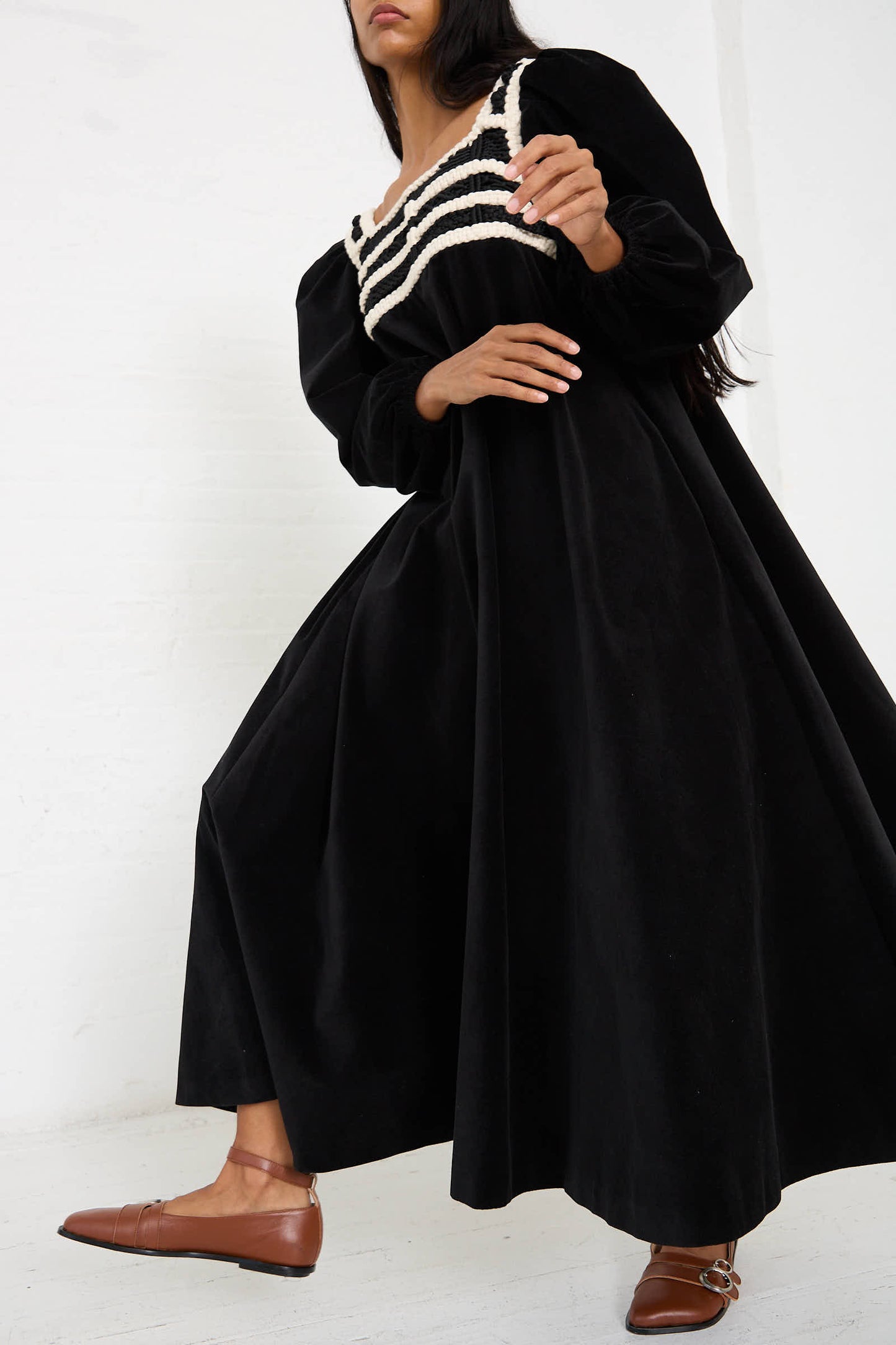 Person standing and posing in a Niccolò Pasqualetti Velvet Corpetto Dress in Black, featuring a relaxed fit with a white striped pattern across the chest, and wearing brown loafers.