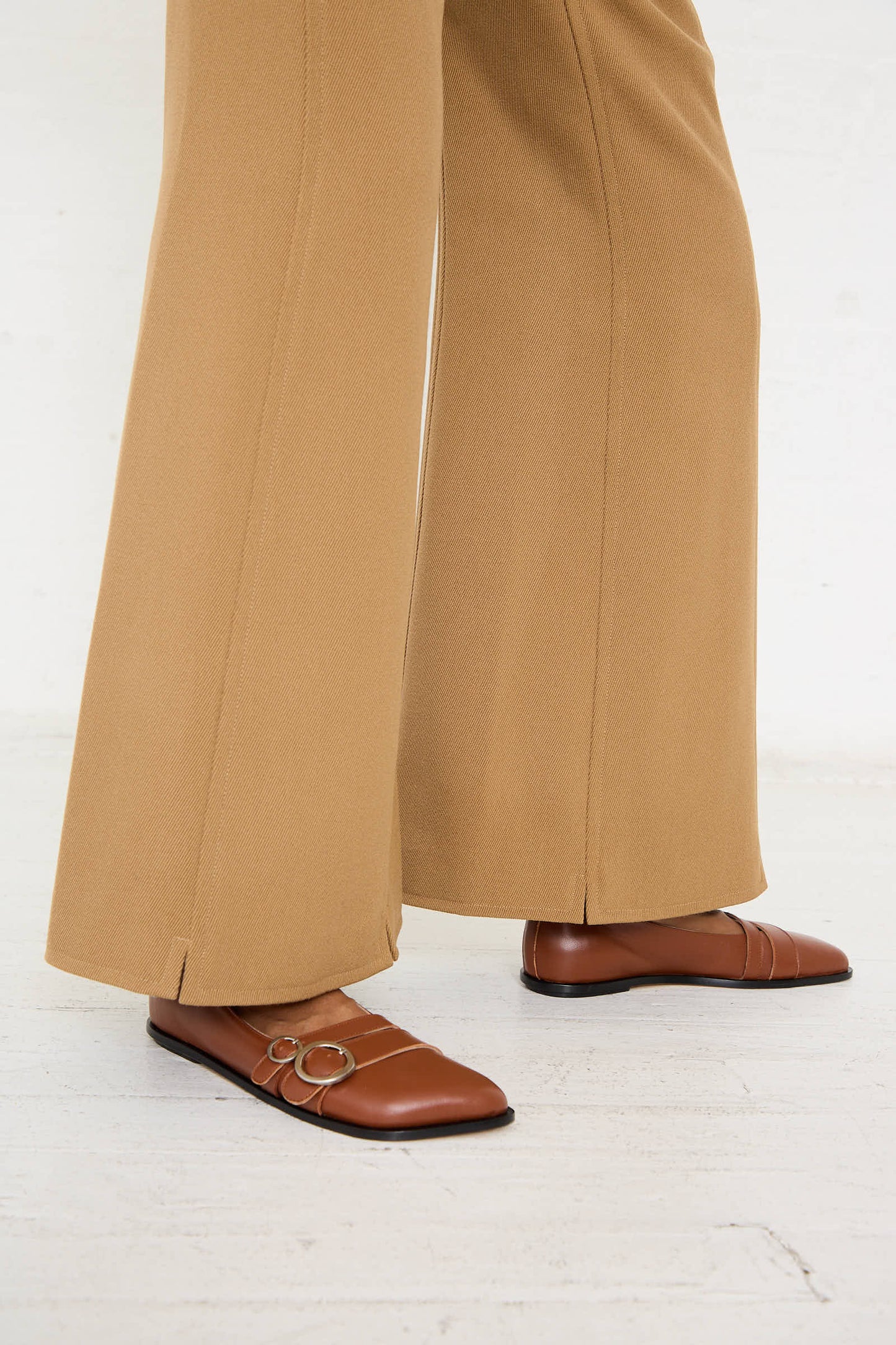 A person wearing Niccolò Pasqualetti's Wool Drill Tegola Trouser in Antique Bronze and brown leather loafers stands on a white floor.