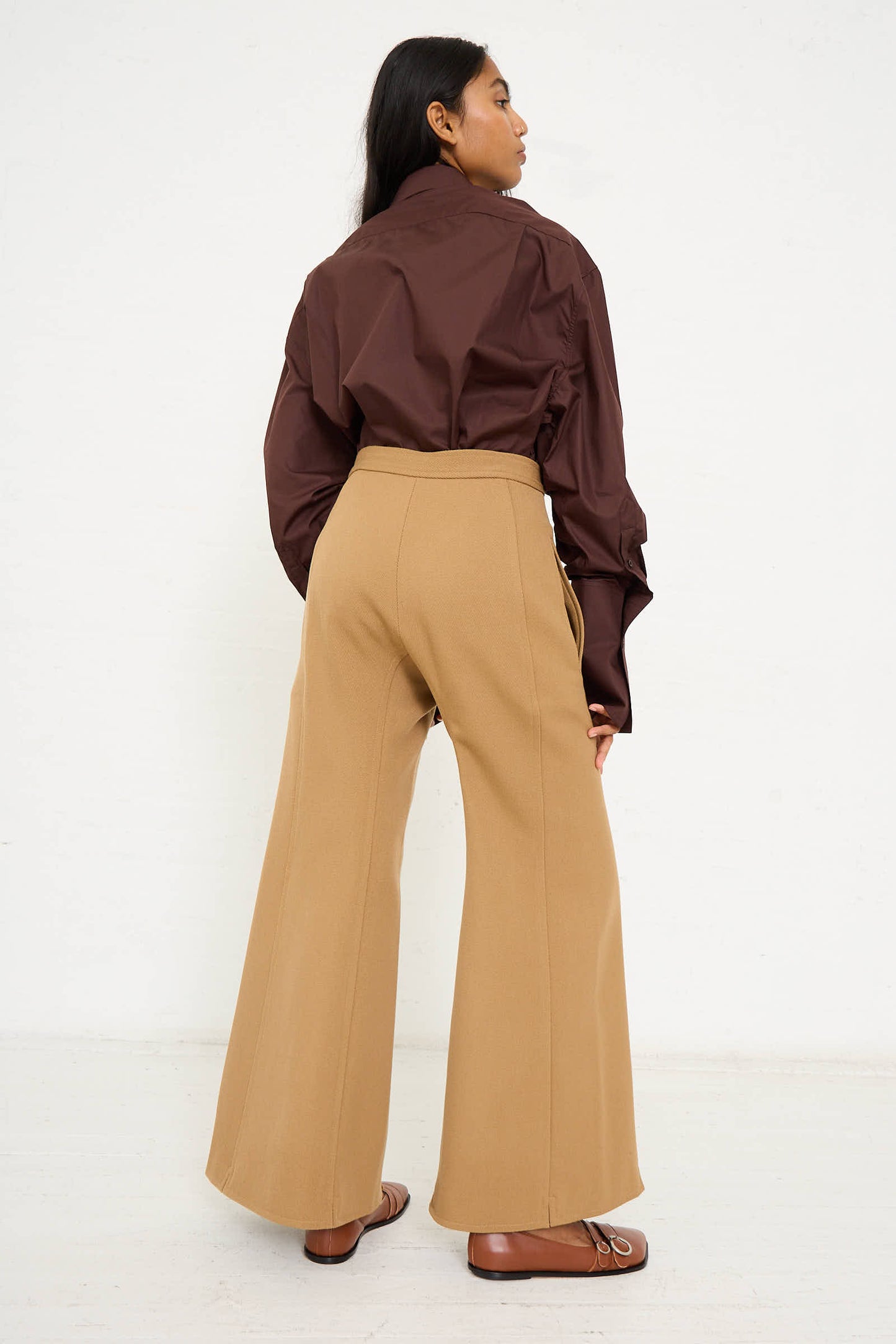 A woman stands facing away, wearing a Niccolò Pasqualetti Wool Drill Tegola Trouser in Antique Bronze.