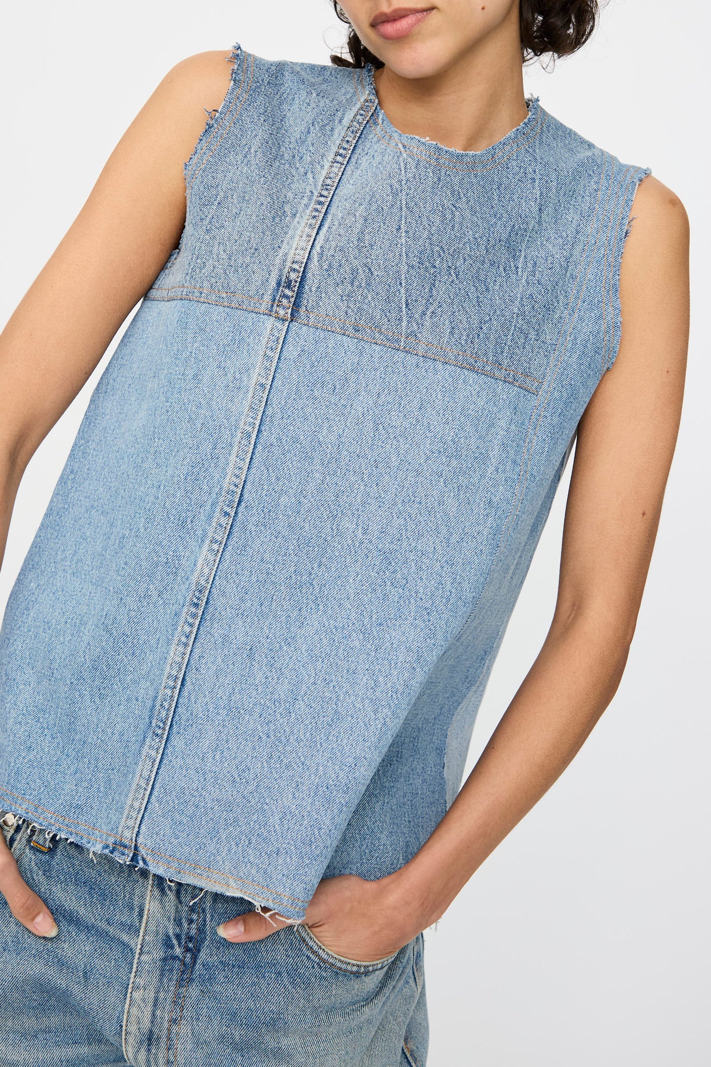Model wears the Niccolò Pasqualetti Salvaged Jean Patchwork Carta Tank in Blue Denim, featuring raw edge hems, paired with light blue jeans; shown from shoulders to hips against a plain background.