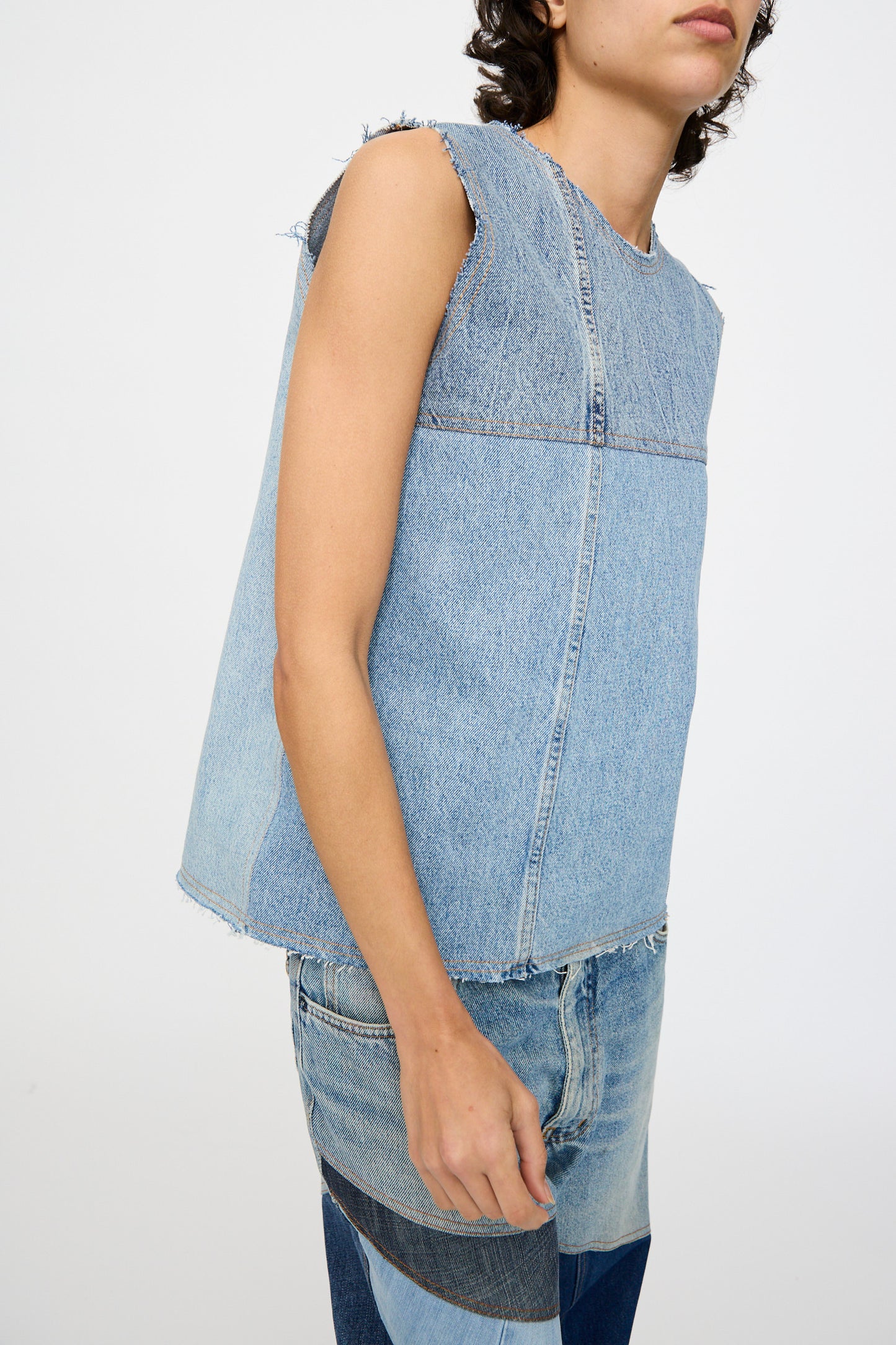 A model wears the Niccolò Pasqualetti Salvaged Jean Patchwork Carta Tank in blue denim, featuring raw edge hems, paired with patchwork jeans, posed against a plain white background.