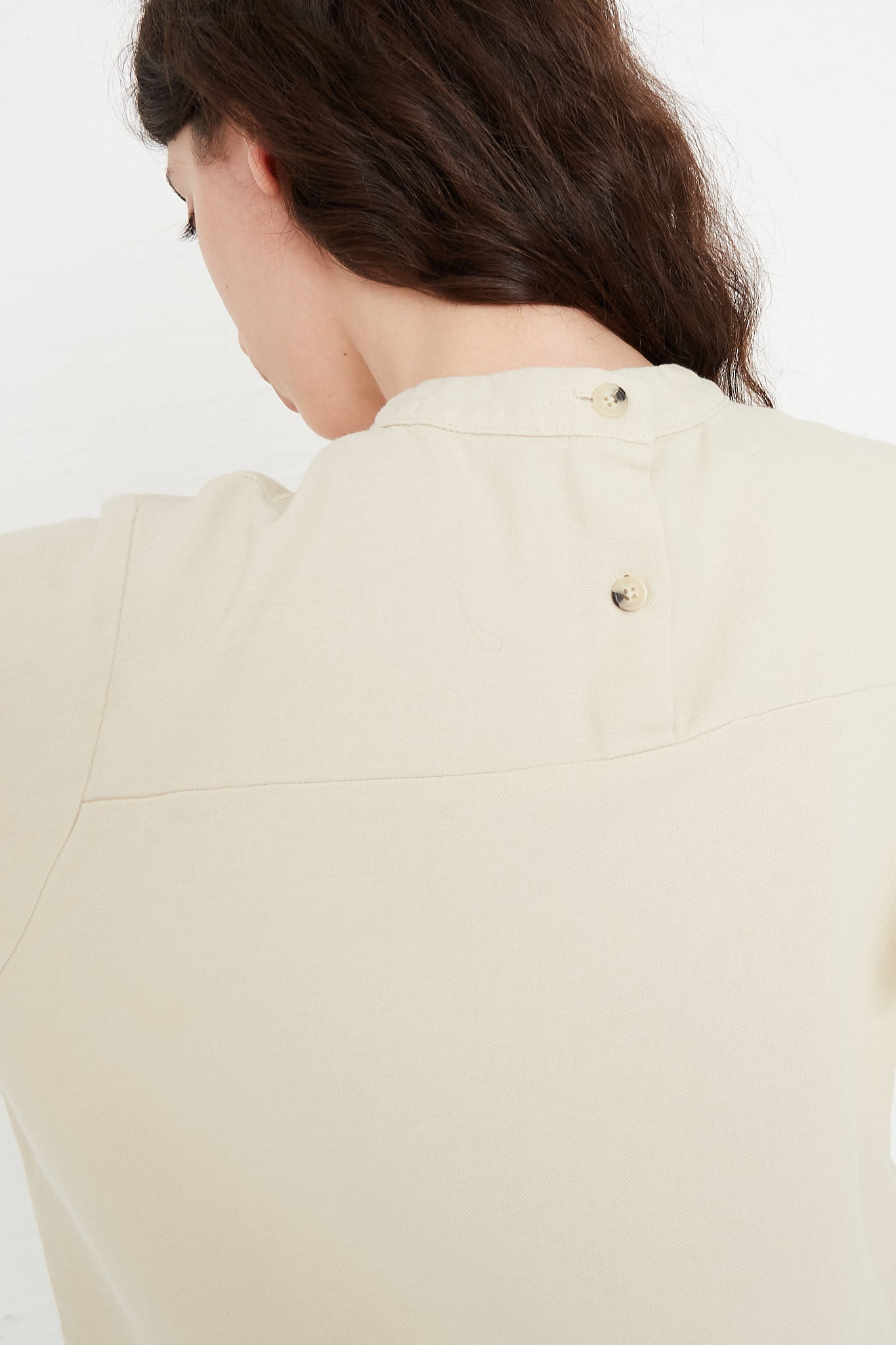 The view of a woman wearing the Black Crane Cotton Twill Puff Sleeve Blouse in Ivory. Back view and up close. 