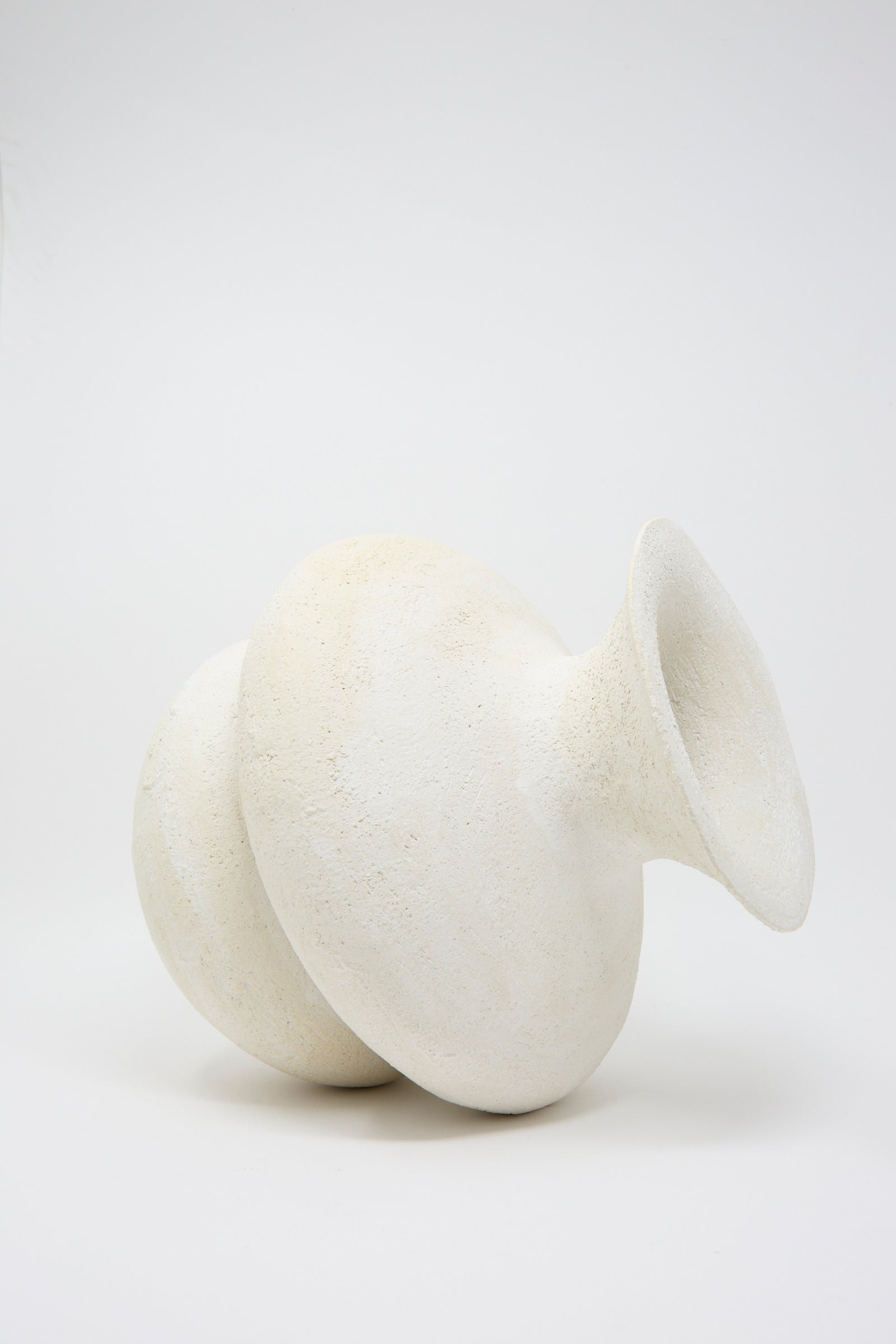 The Double Bottom Vessel, a handmade white ceramic piece by Oatmeal, features a round abstract design and rests on its side against a plain background.