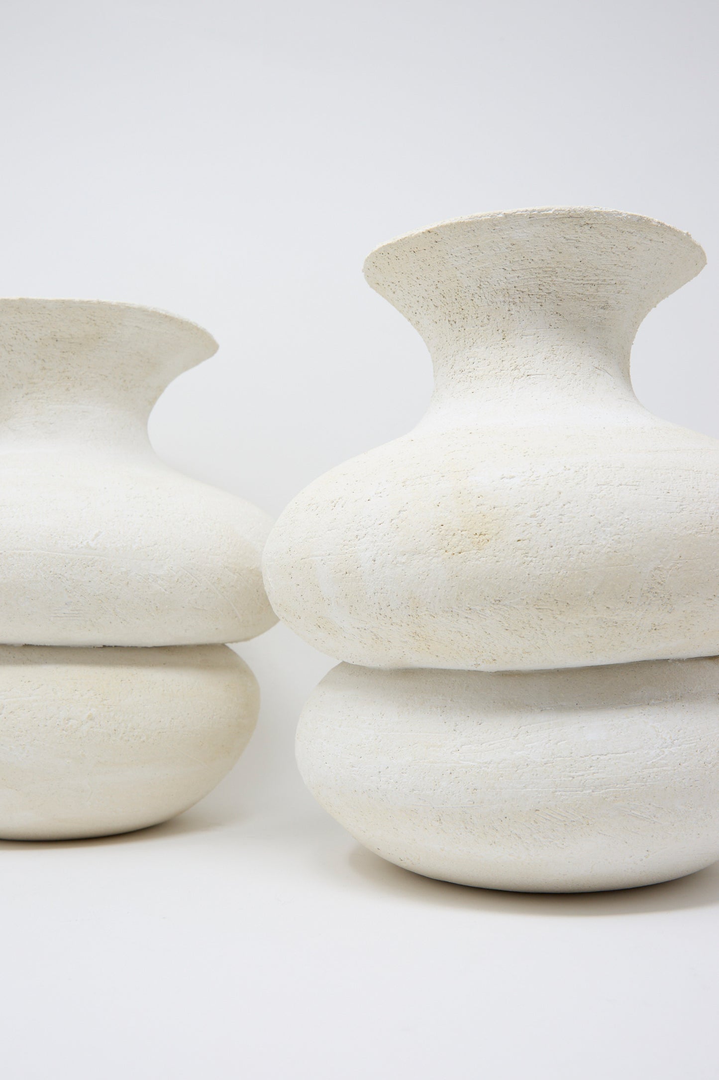 The Double Bottom Vessel by Oatmeal highlights Pennsylvania craftsmanship with its textured, off-white ceramic design, featuring wide, rounded shapes and narrow openings against a plain background. Two vases are pictured. 