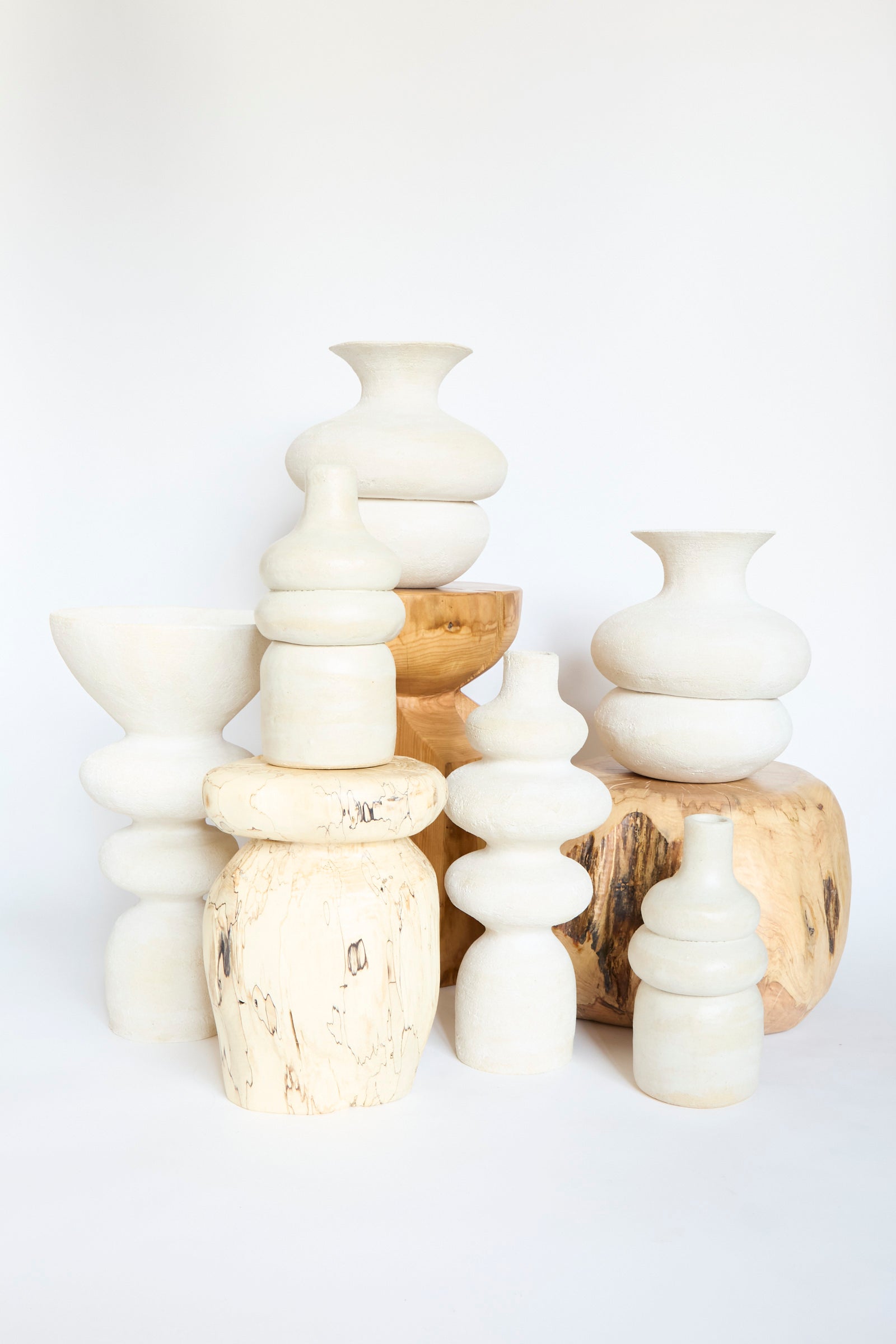 A display featuring the Double Bottom Vessel by Oatmeal, alongside other uniquely shaped handmade white ceramic vases, set against a plain backdrop.