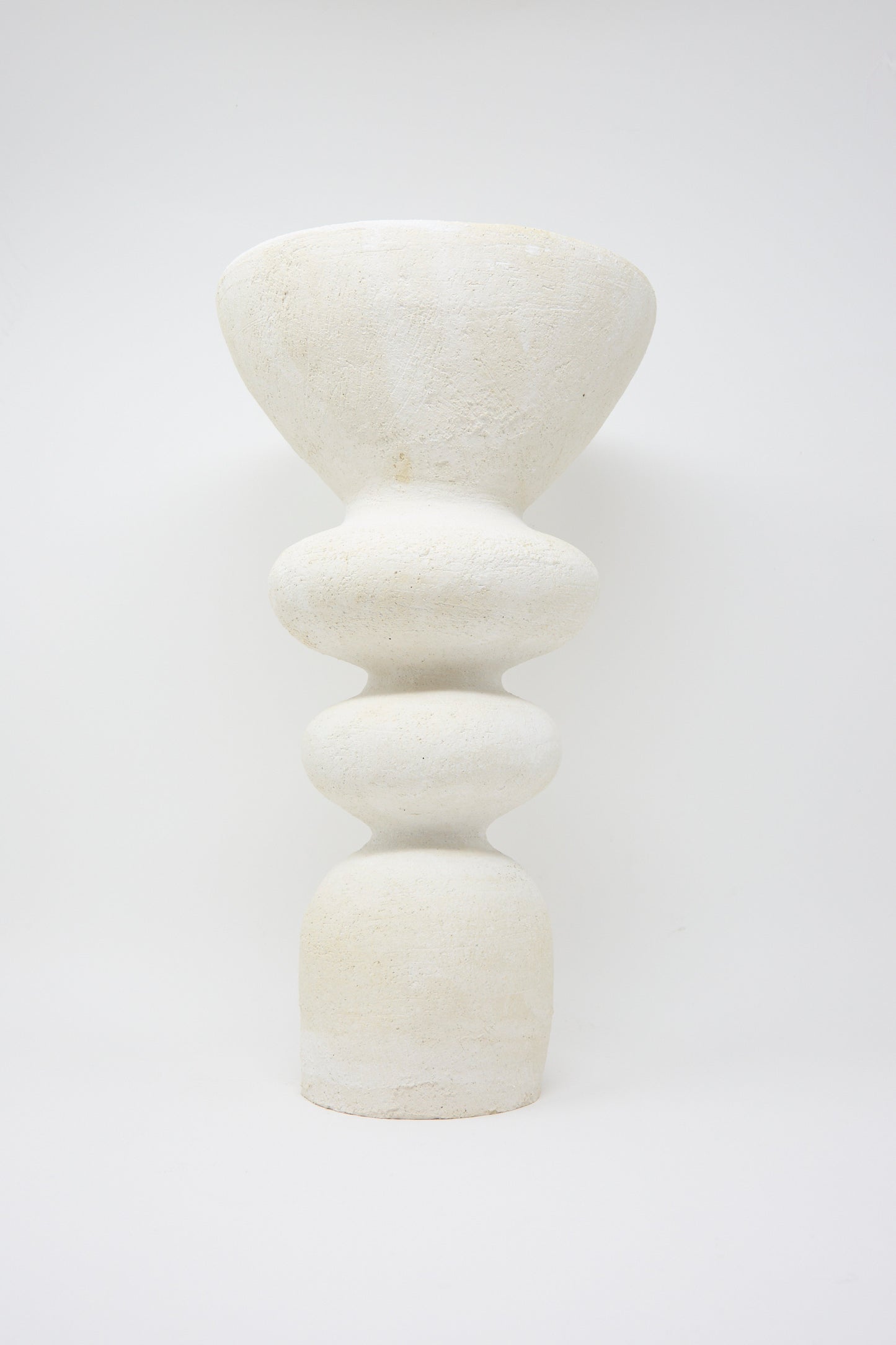 Introducing the Monolith Vessel by Oatmeal, a sculptural ceramic piece handmade in Pennsylvania. This vessel features a textured surface with a wide top and multiple rounded, stacked forms in white, against a plain background. 