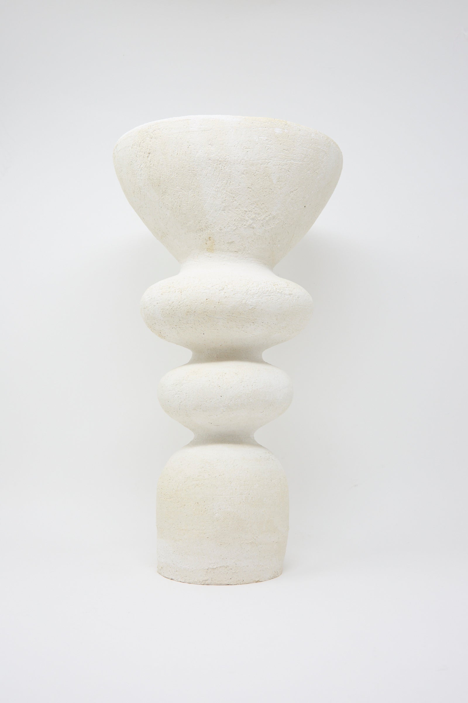 Introducing the Monolith Vessel by Oatmeal, a sculptural ceramic piece handmade in Pennsylvania. This vessel features a textured surface with a wide top and multiple rounded, stacked forms in white, against a plain background. 