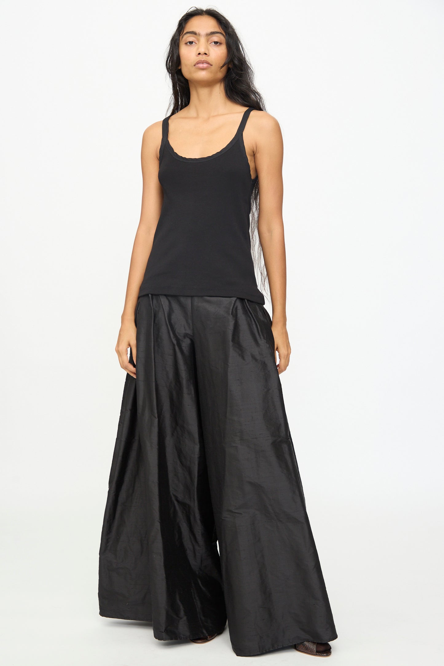 Wearing the Billie Singlet in Black by Olivia Cashmore and wide-leg black pants, a person stands against a plain white background.