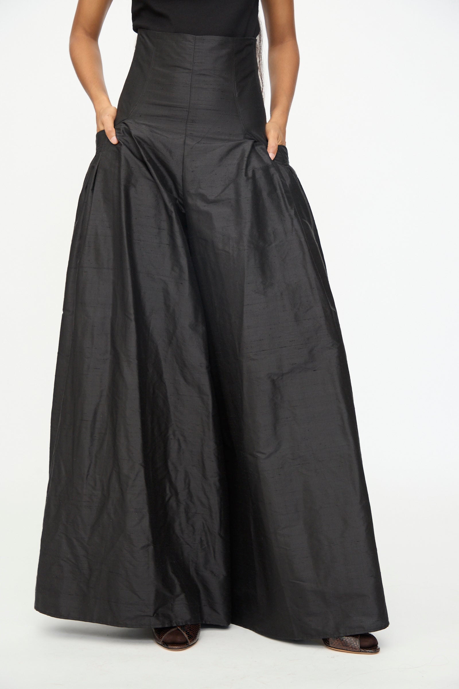 Wearing the Olivia Cashmore Robbie Pant in Black, featuring a high-waisted, wide-leg silhouette and convenient pockets, the model poses against a plain white background.