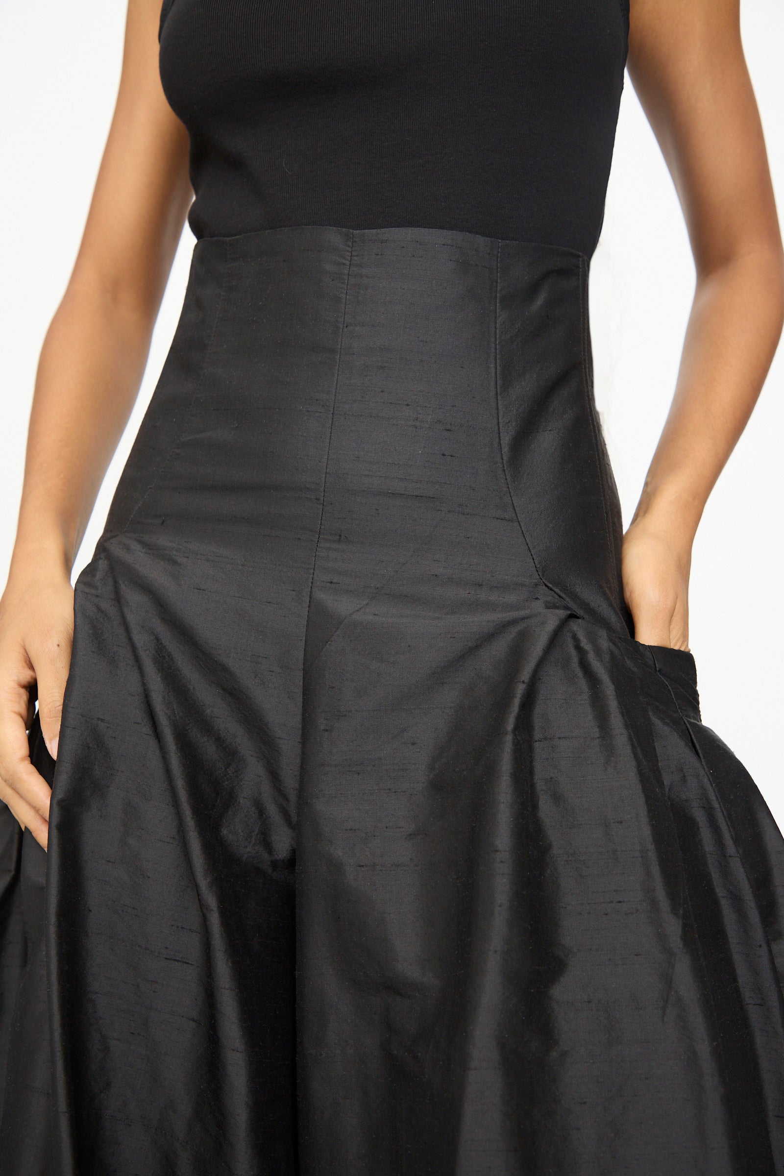 Wearing the Olivia Cashmore Robbie Pant in Black, this person has their hands in the pockets of the high-waisted silhouette.