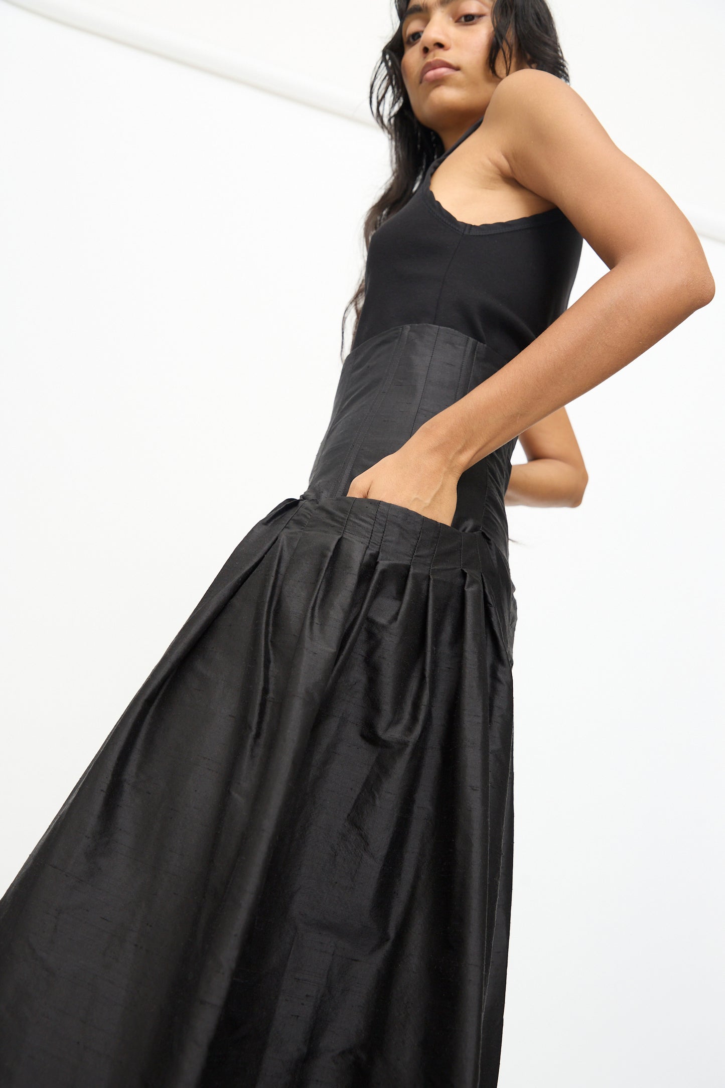 A person wearing the Olivia Cashmore Robbie Pant in Black, paired with a black sleeveless top and posing with one hand in the pocket, stands against a plain white background.