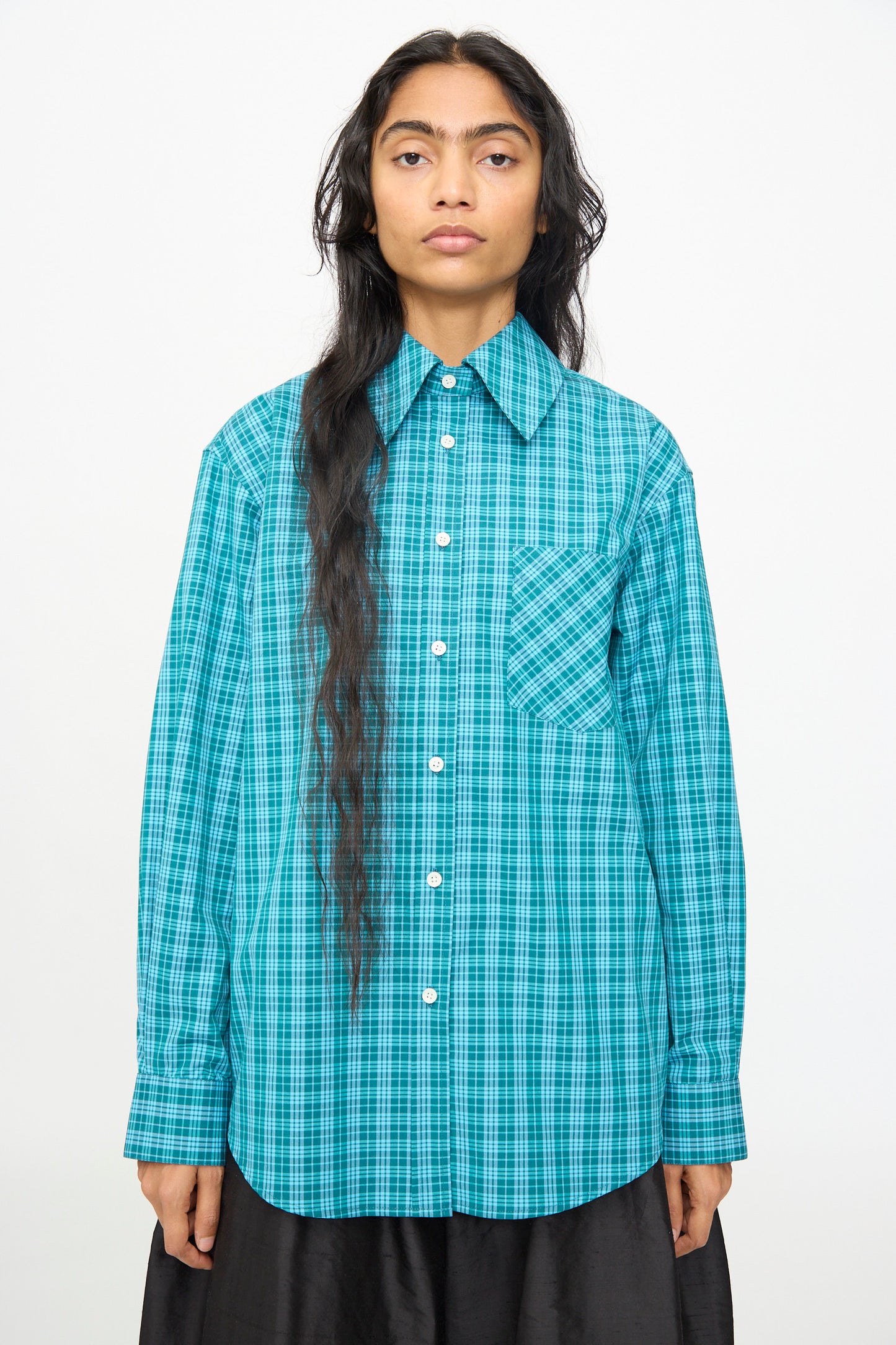 A person wears the Olivia Cashmore Rufus Shirt in Blue Green Check—a cotton, long-sleeve, button-up shirt with a front pocket—standing against a plain white background. This stylish piece is proudly made in New Zealand.