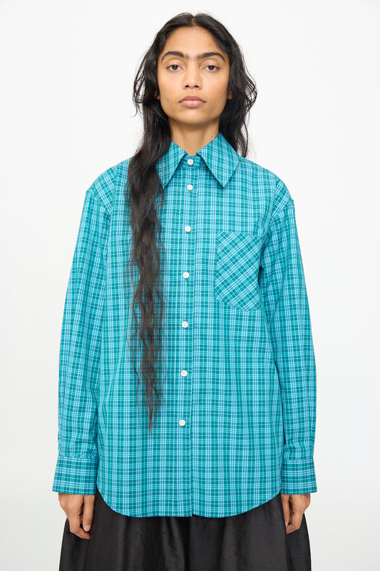 A person wears the Olivia Cashmore Rufus Shirt in Blue Green Check—a cotton, long-sleeve, button-up shirt with a front pocket—standing against a plain white background. This stylish piece is proudly made in New Zealand.