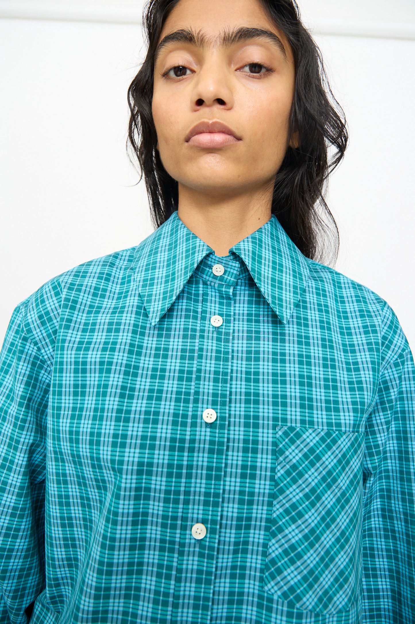 A person stands against a plain white background wearing the Olivia Cashmore Rufus Shirt in Blue Green Check.