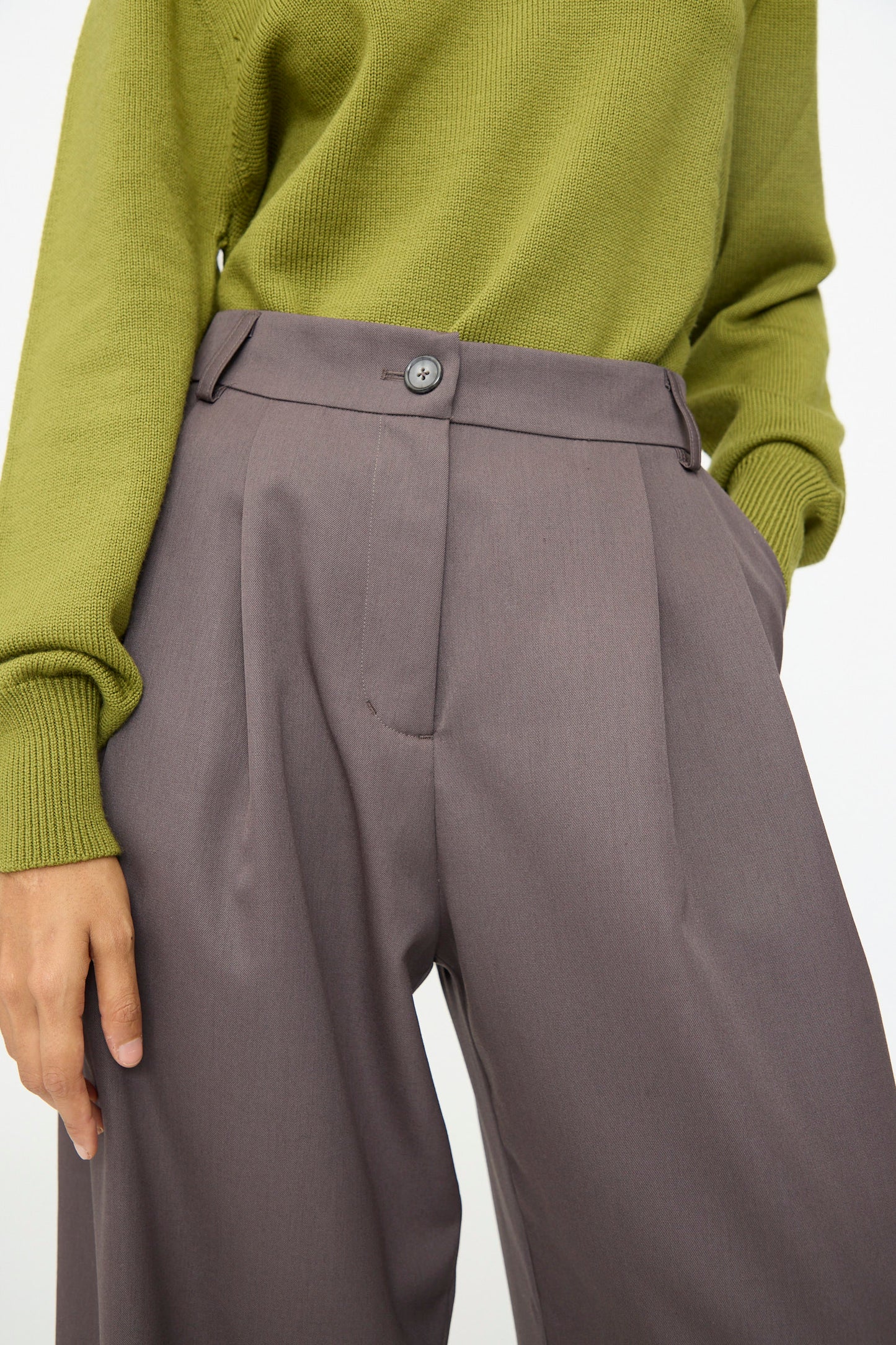 A person wears the Olivia Cashmore Wool Marco Pant in Mud, styled high-waisted with a relaxed wide-leg silhouette and hands in pockets for an effortlessly tailored look, paired with an olive green sweater.