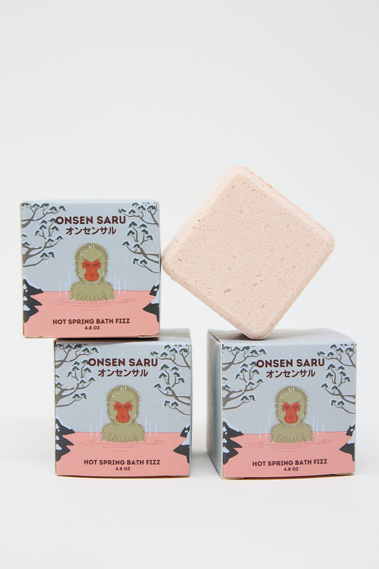 Three boxes of Onsen Saru Hot Spring Bath Fizz with one pink bath fizz cube above the boxes, displayed against a white background.