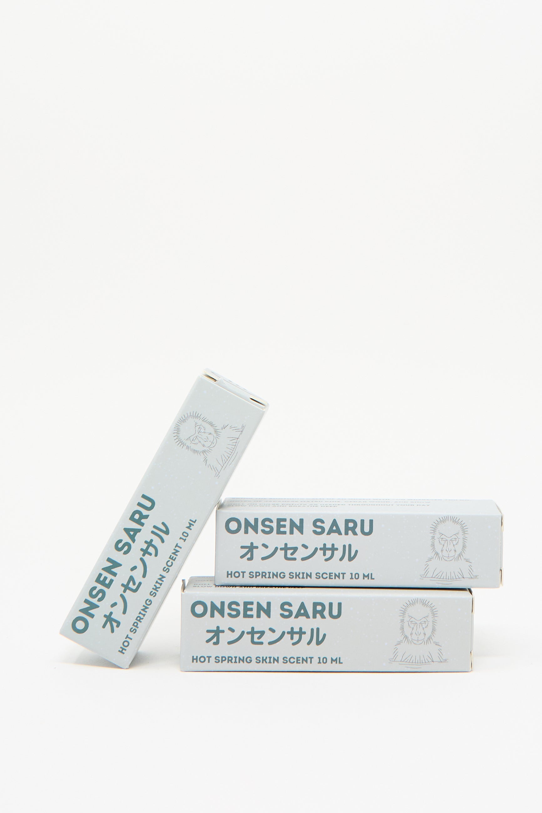 Three boxes of Onsen Saru's Hot Spring Skin Scent, each containing 10 ml, showcase minimalist packaging adorned with Japanese text and a monkey illustration. This natural perfume embodies the essence of a Japanese Matsu pine, delivering a refreshing unisex fragrance.