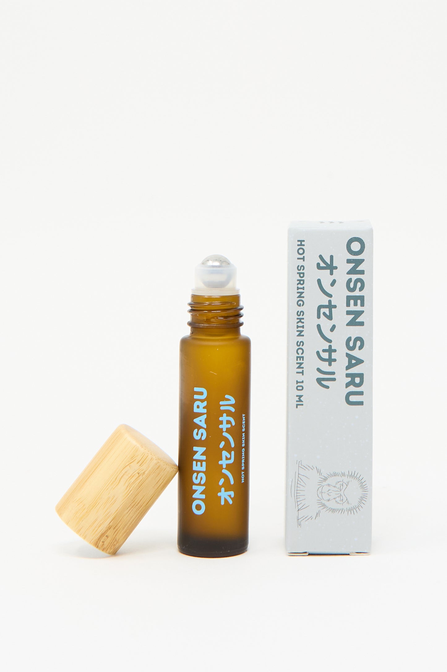 Amber glass roll-on bottle featuring a wooden cap, branded "Hot Spring Skin Scent" by Onsen Saru, emanates the natural fragrance of Japanese Matsu pine. Accompanied by a matching box with cohesive branding, this unisex scent encapsulates the calming essence of a peaceful spa experience.