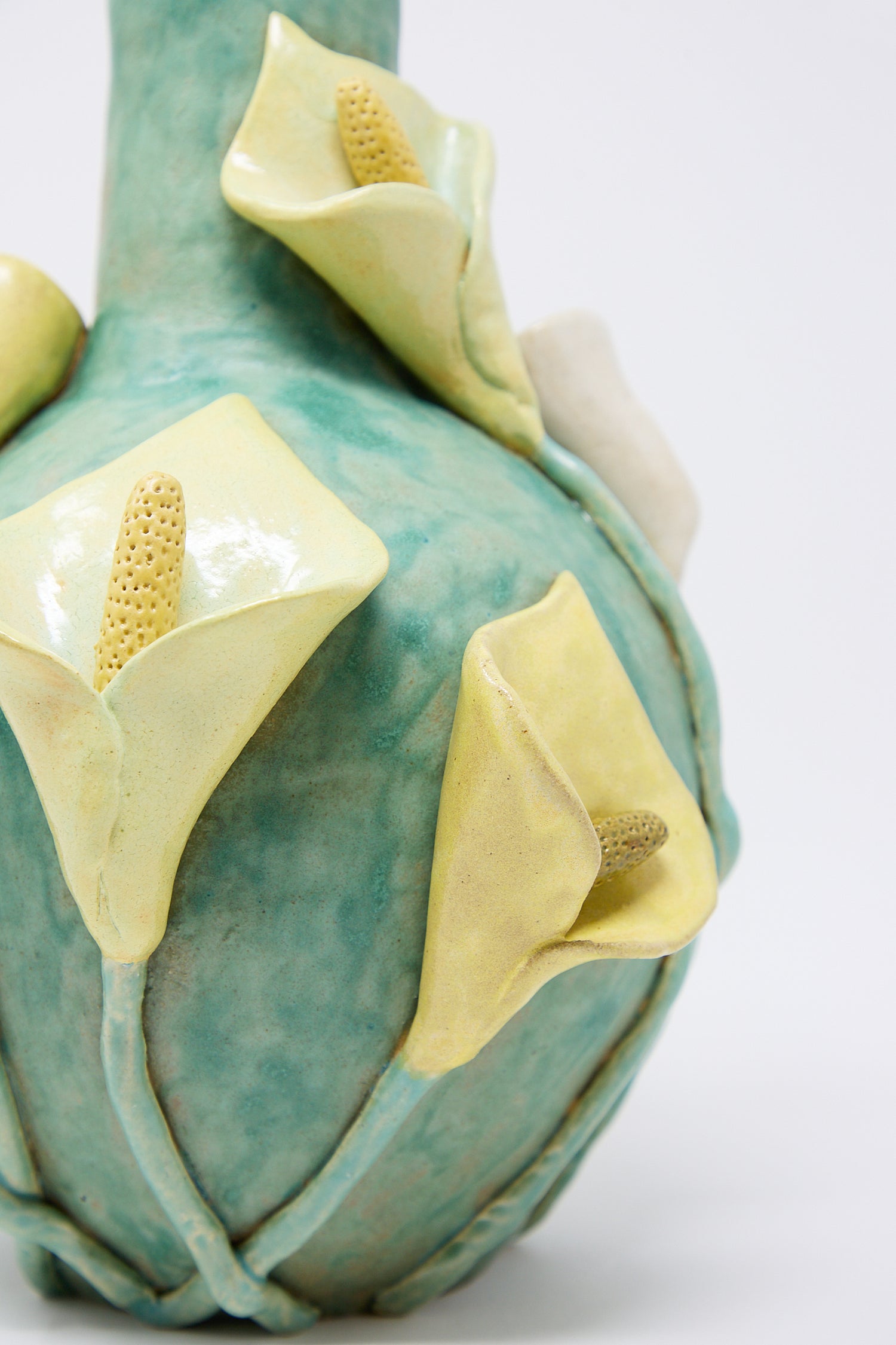 Close-up of a glazed stoneware Calla Vase by Pearce Williams with a textured turquoise surface and three-dimensional yellow calla lily decorations.