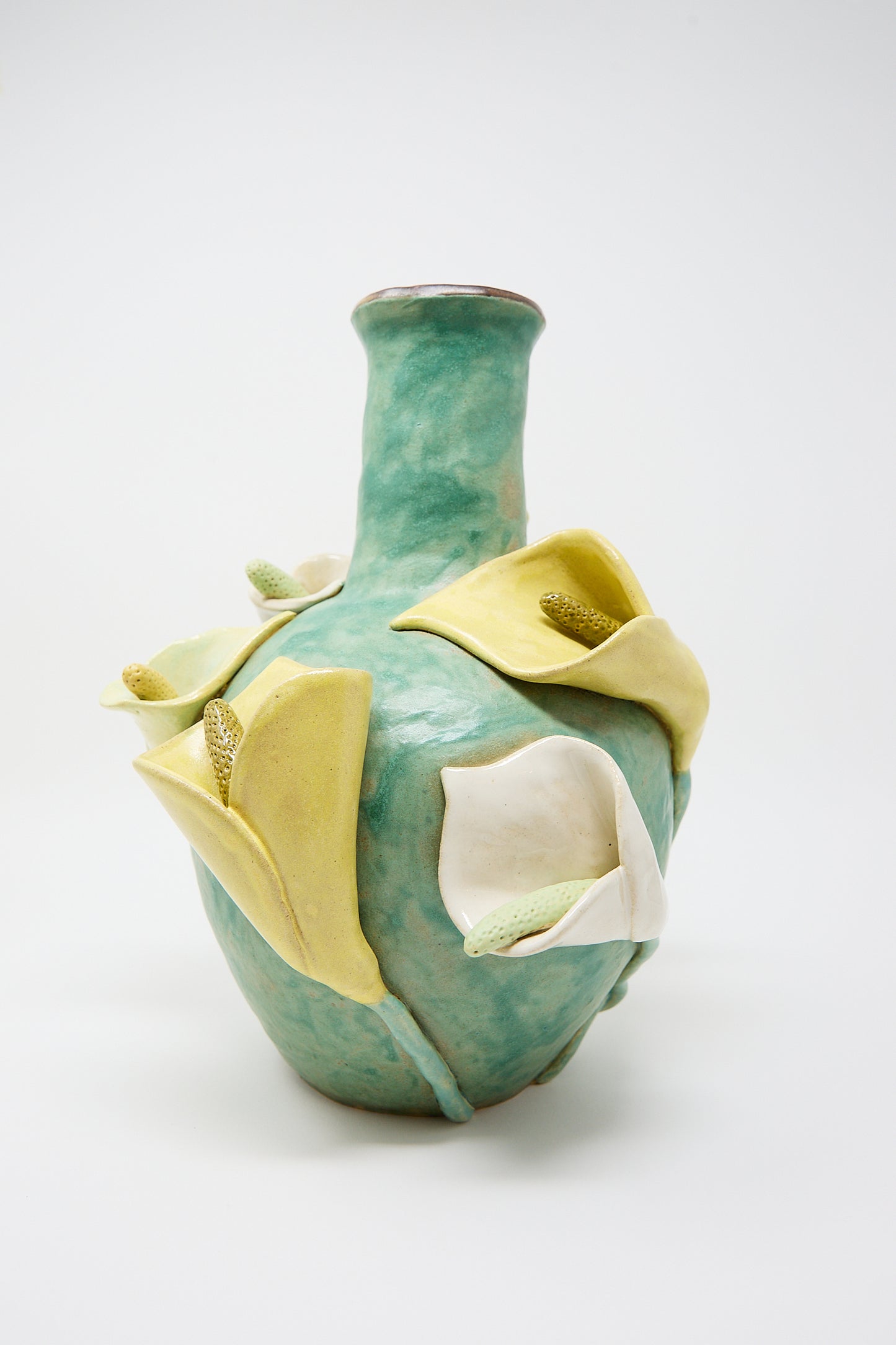 A glazed stoneware Calla Vase from Pearce Williams with a turquoise glaze, adorned with sculpted, yellow-white calla lilies and textured details, set against a white background.