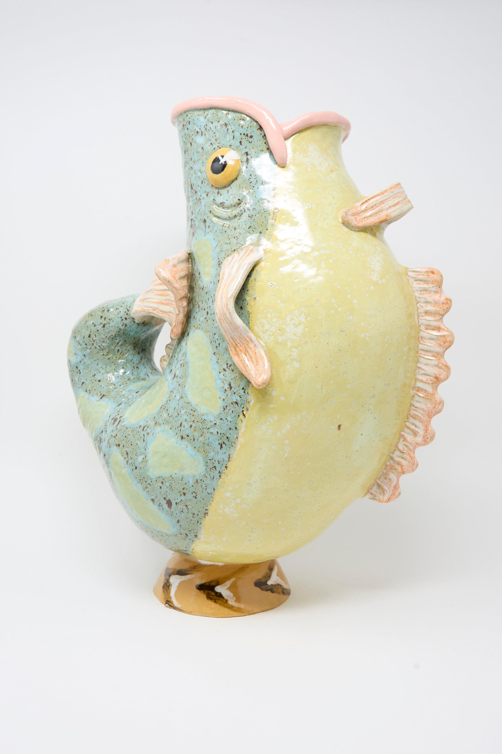The Pearce Williams Fish Pitcher II is a ceramic vase, handmade and painted with green, yellow, and pink glazes, displayed against a plain white background for a colorful decorative accent.