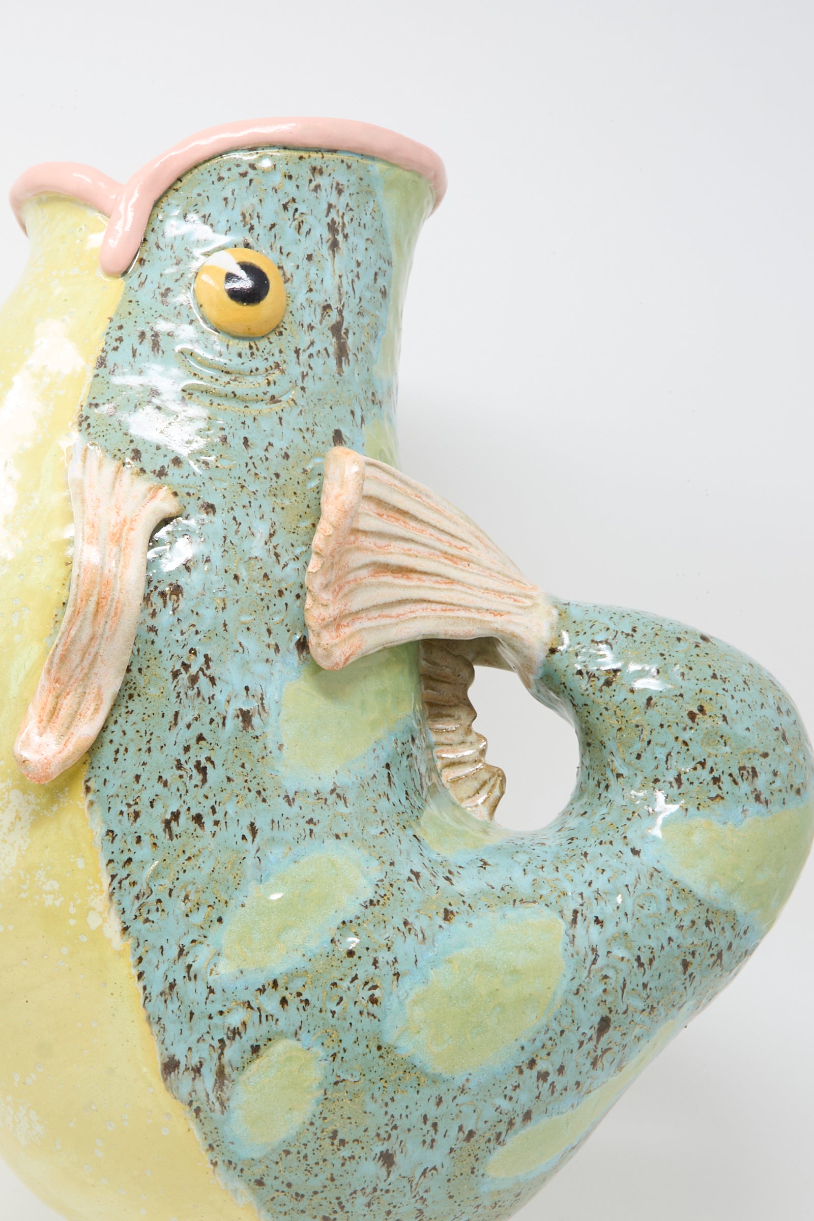 Close-up of Pearce Williams' Fish Pitcher II, a colorful decorative vase with textured fins, a spotted blue-green body, and a yellow underbelly, shaped and painted like a fish.