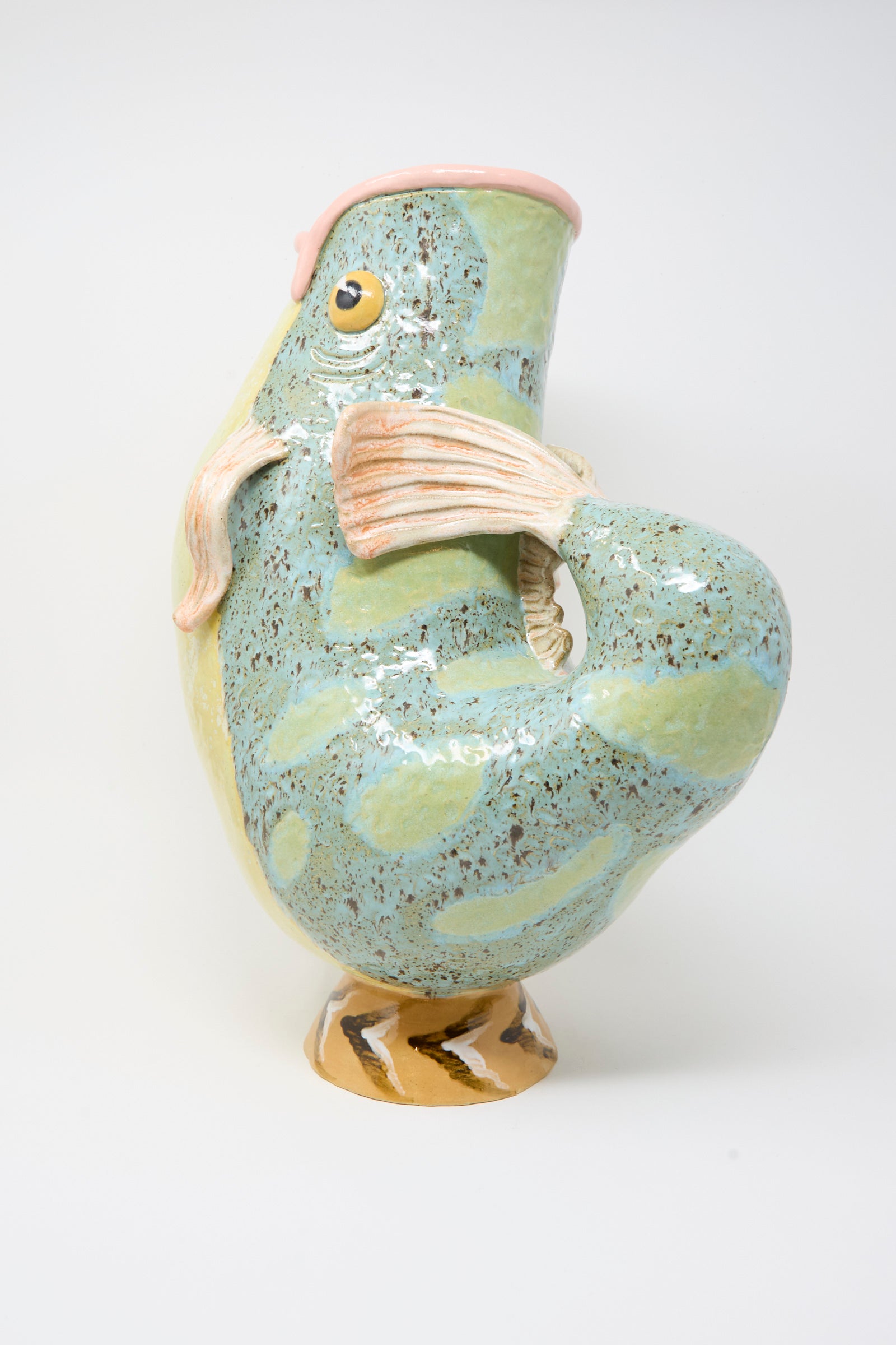 The Fish Pitcher II by Pearce Williams is a handmade ceramic vase with a blue-green speckled glaze, curled tail handle, and open mouth top—a unique decorative stoneware piece.