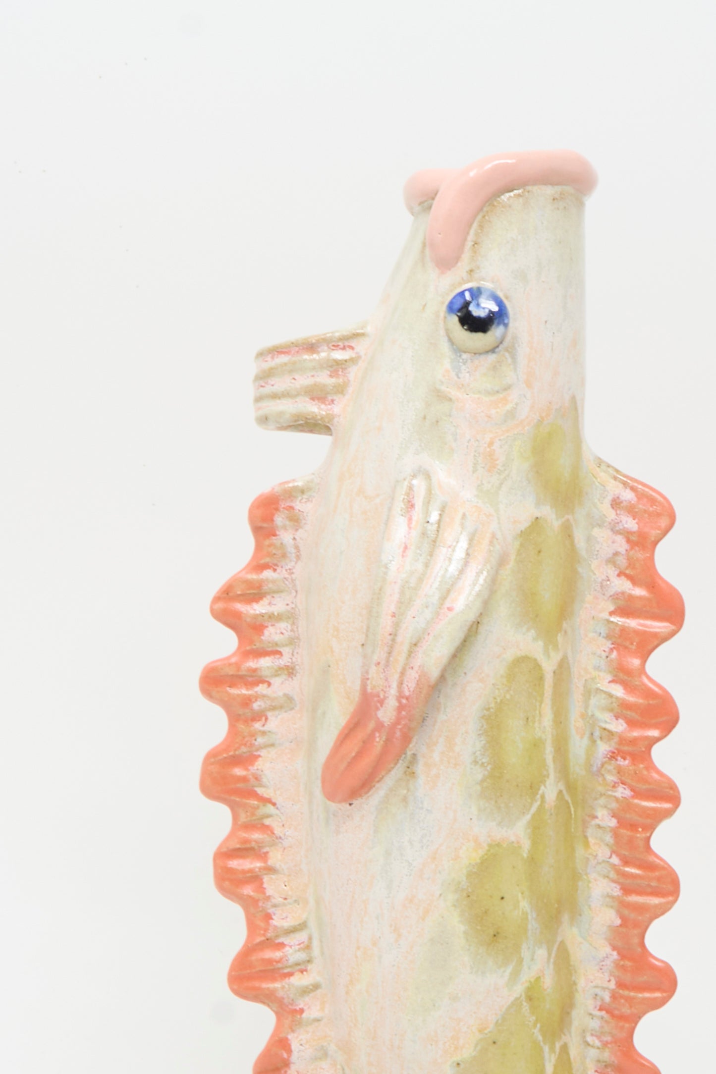 Close-up of the Pearce Williams Fish Vase in Coral II, handmade in New Orleans with a textured ceramic body, orange fins, and a blue eye, displayed against a plain white background.