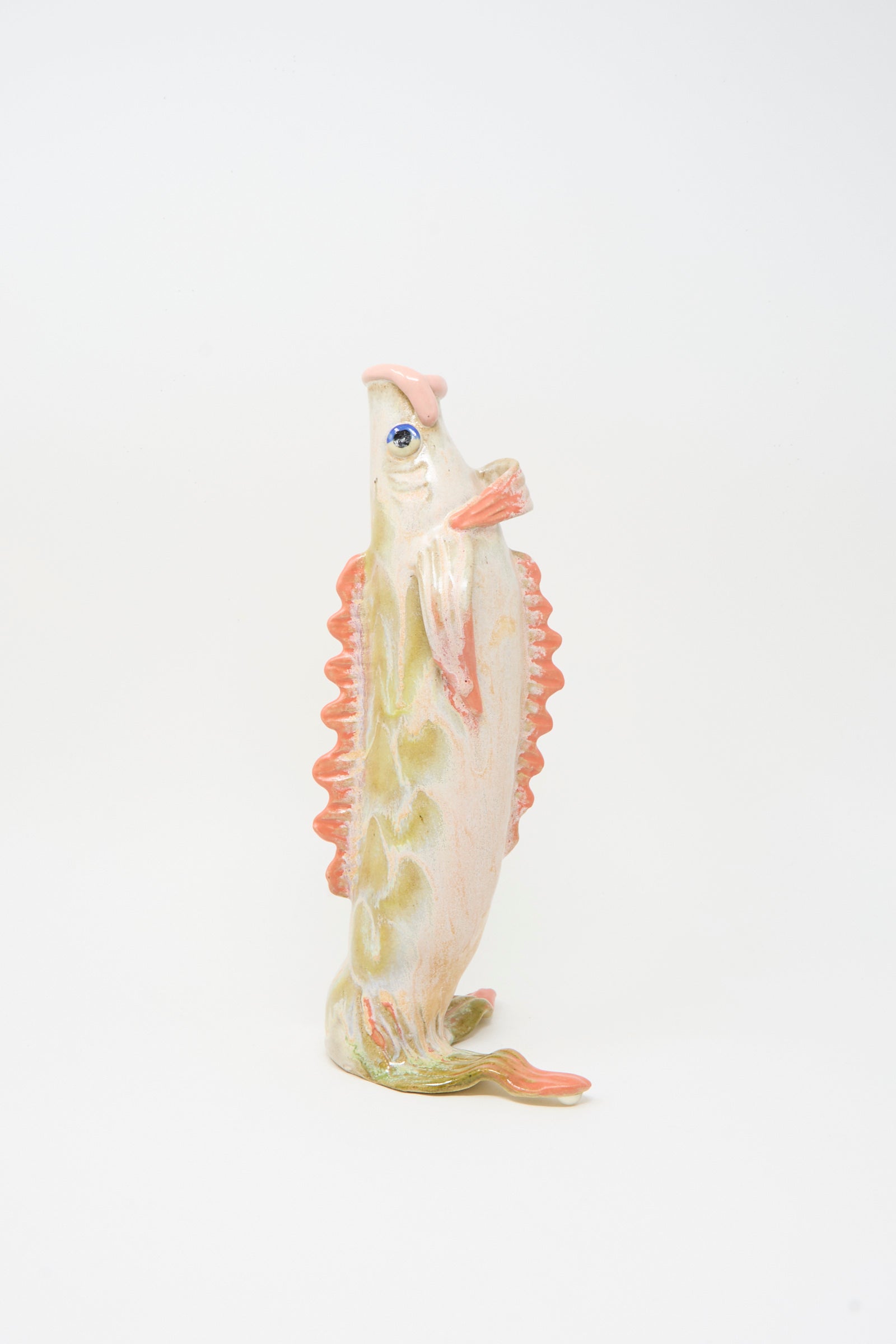 The Pearce Williams Fish Vase in Coral III is a handmade stoneware piece shaped like a fish, with a pale cream, green, and pink glaze, wide open mouth, decorative fins, and stands upright against a white background.