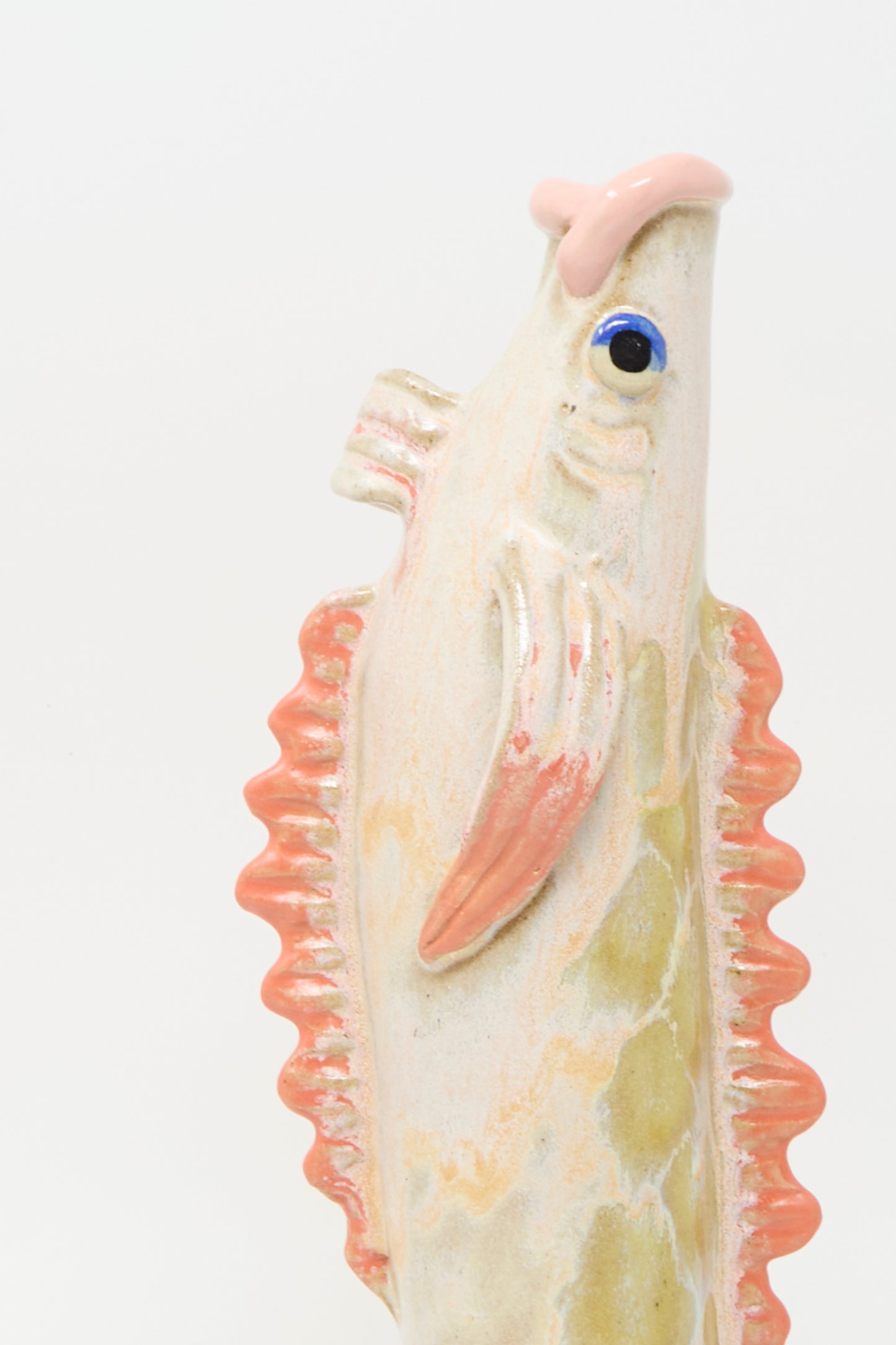 The Pearce Williams Fish Vase in Coral III features a colorful glazed, fish-shaped ceramic body with pink fins and a blue eye, shown against a plain white background.