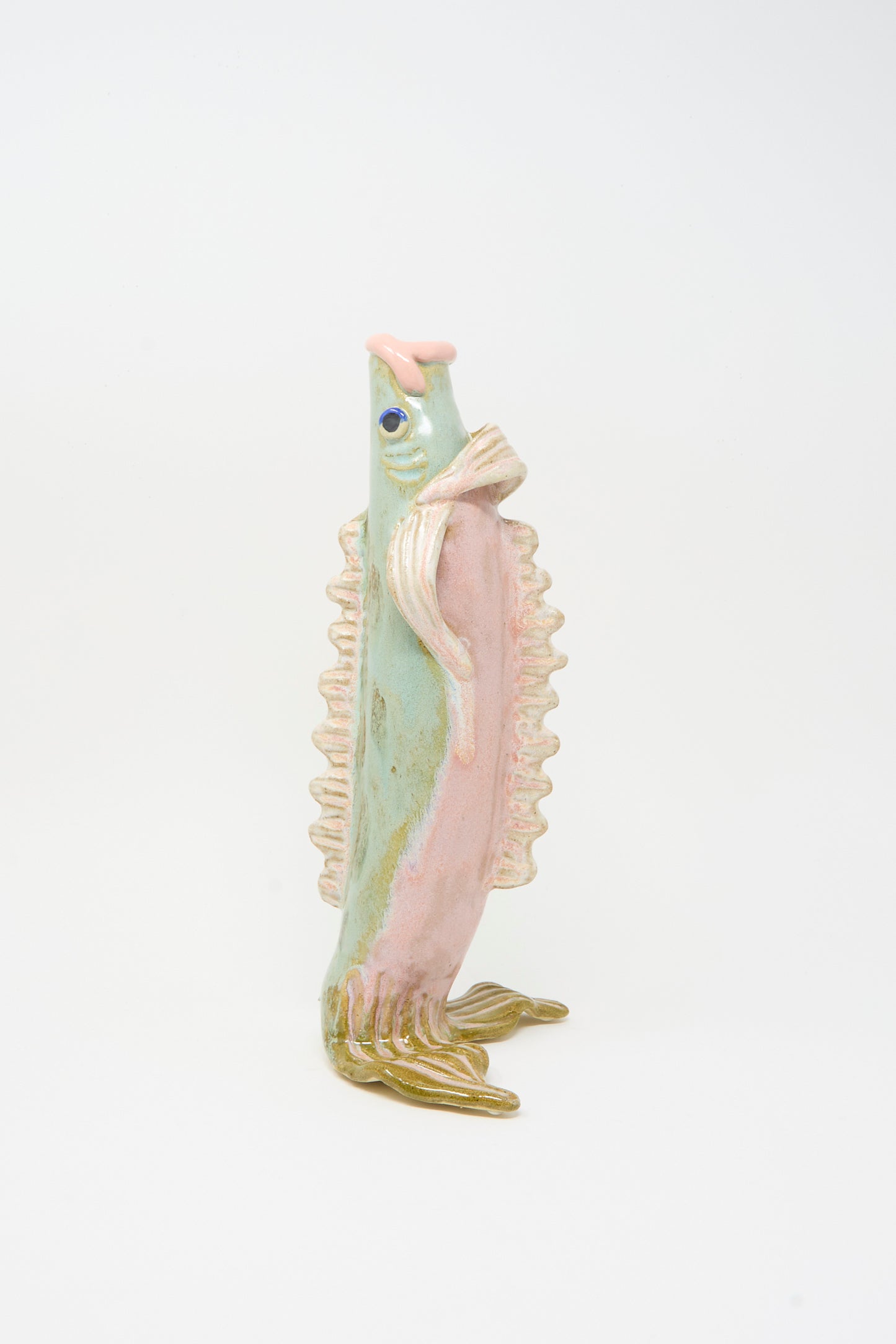 The Pearce Williams Fish Vase in Green, a ceramic sculpture with pastel pink, green, and cream details, stands upright on its fins.