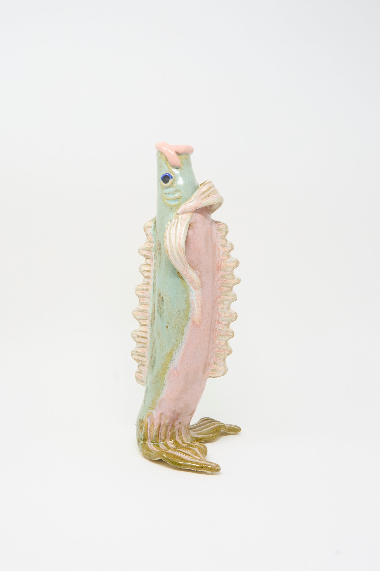 The Pearce Williams Fish Vase in Green, a ceramic sculpture with pastel pink, green, and cream details, stands upright on its fins.