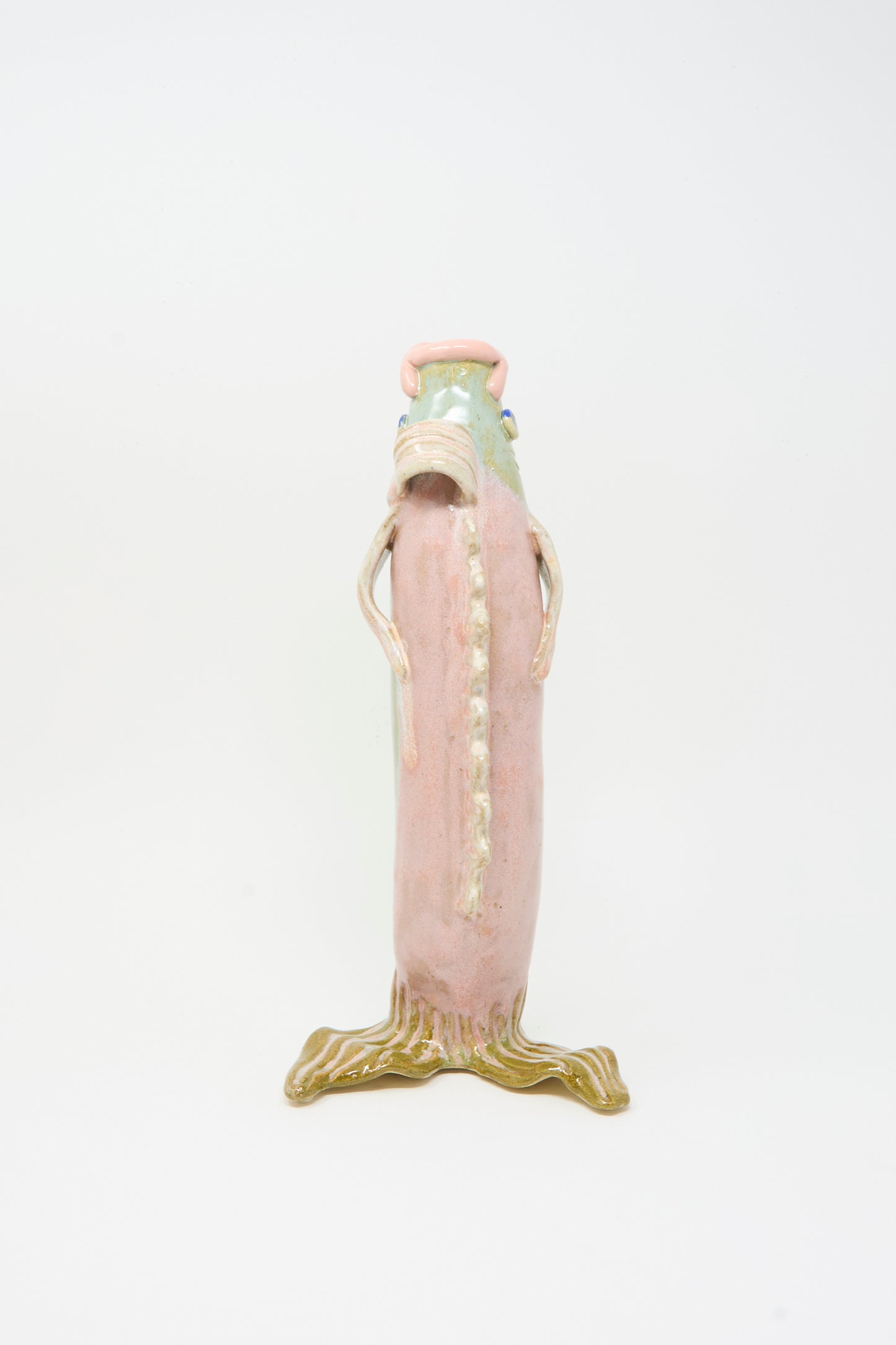 The Fish Vase in Green by Pearce Williams features a tall, pinkish ceramic figure with a textured surface, small arms, and a greenish root-like base, evoking the look of handmade stoneware against a plain white background.