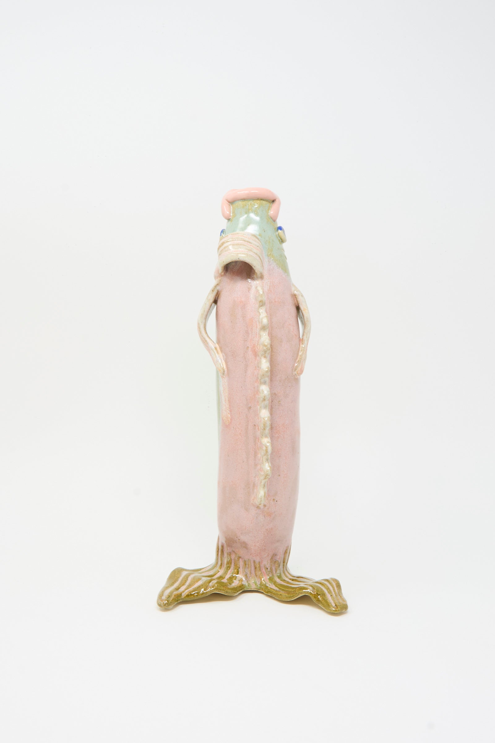 The Fish Vase in Green by Pearce Williams features a tall, pinkish ceramic figure with a textured surface, small arms, and a greenish root-like base, evoking the look of handmade stoneware against a plain white background.