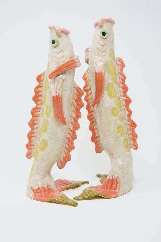 Two whimsical ceramic koi fish sculptures standing upright, decorated with pastel pink, green, and yellow accents on a white background.