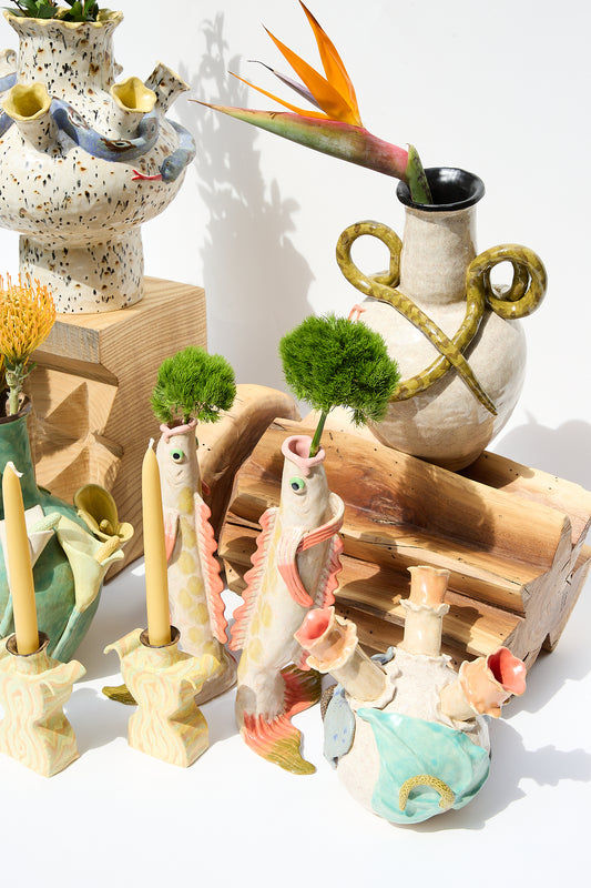 A collection of colorful, whimsical hand-made ceramics including sea creatures and abstract Snake Amphora Vases by Pearce Williams, displayed alongside wooden elements and plants.