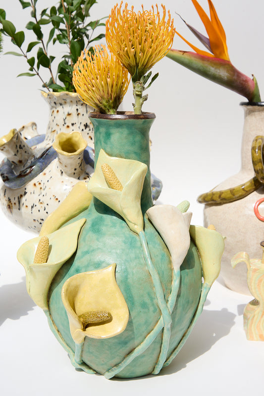 A vibrant glazed stoneware Calla Vase by Pearce Williams sculpted to resemble blooming flowers, flanked by other quirky pottery pieces holding bright Calla lilies.