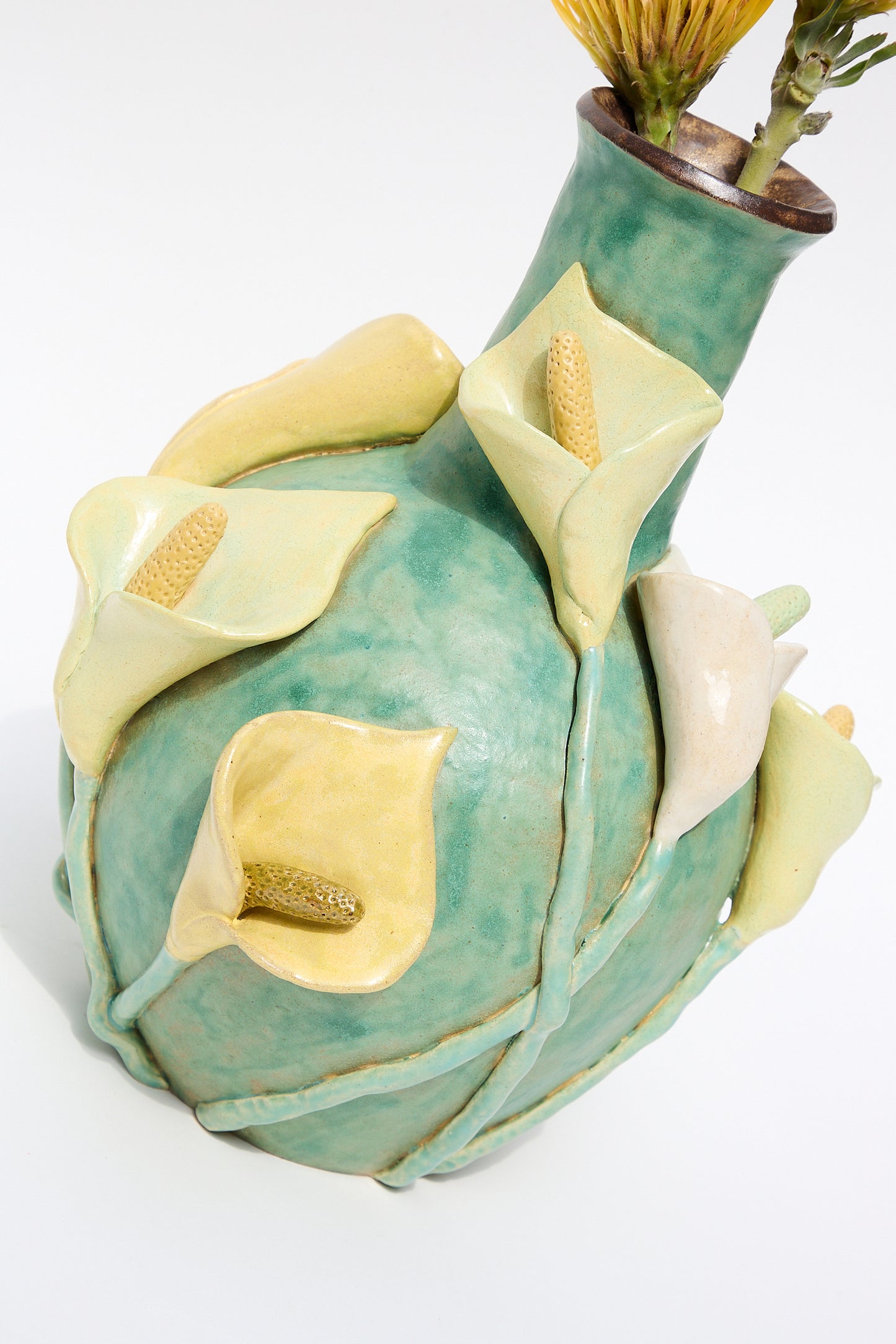 Sentence with replaced product:
A glazed stoneware Pearce Williams Calla Vase resembling an artichoke with green and pale yellow tones, featuring intricate textures and a few Calla lilies protruding from the top.