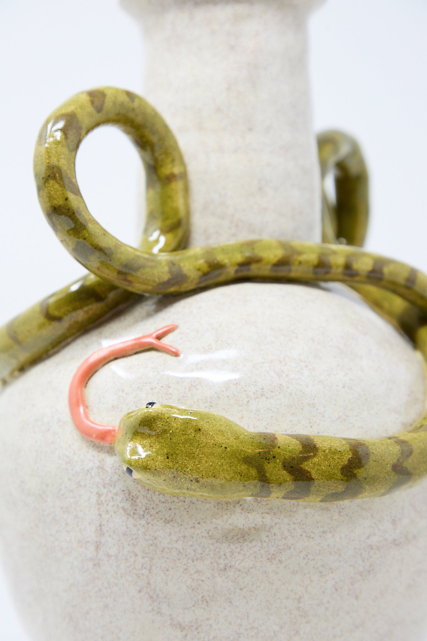 Close-up of a glazed stoneware Snake Amphora Vase with a textured finish, featuring a sculpted green snake with red tongue wrapped around its neck by Pearce Williams.