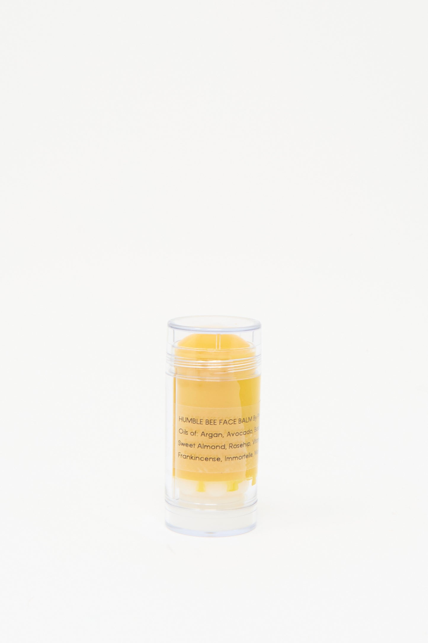 A clear cylindrical container holds a yellow balm labeled "Humble Bee Face & Body Balm" by Photerian, crafted as a moisturizing salve with beeswax and proudly made in Washington State.