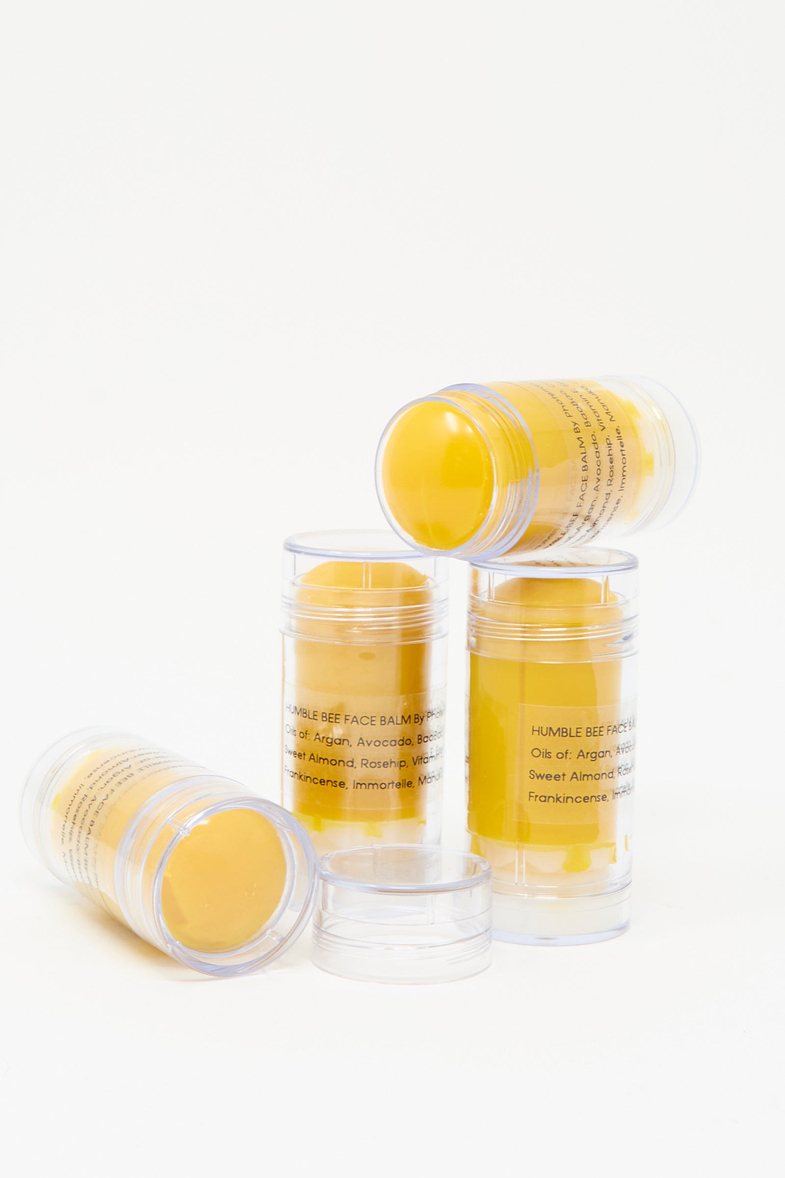 Four tubes of Humble Bee Face & Body Balm by Photerian, enriched with beeswax, are on a white background. Two stand upright while the others lean gracefully. Proudly made in Washington state, this balm ensures quality and care.